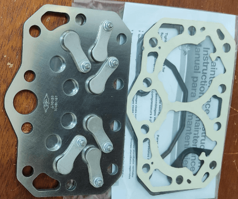 Automotive gasket set on a table, including a metal gasket and a paper gasket, with an instruction manual partially visible.