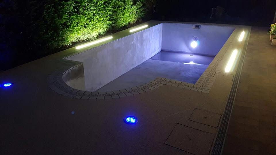 An empty rectangular pool at night, illuminated by blue and white LED lights along the edges and inside.