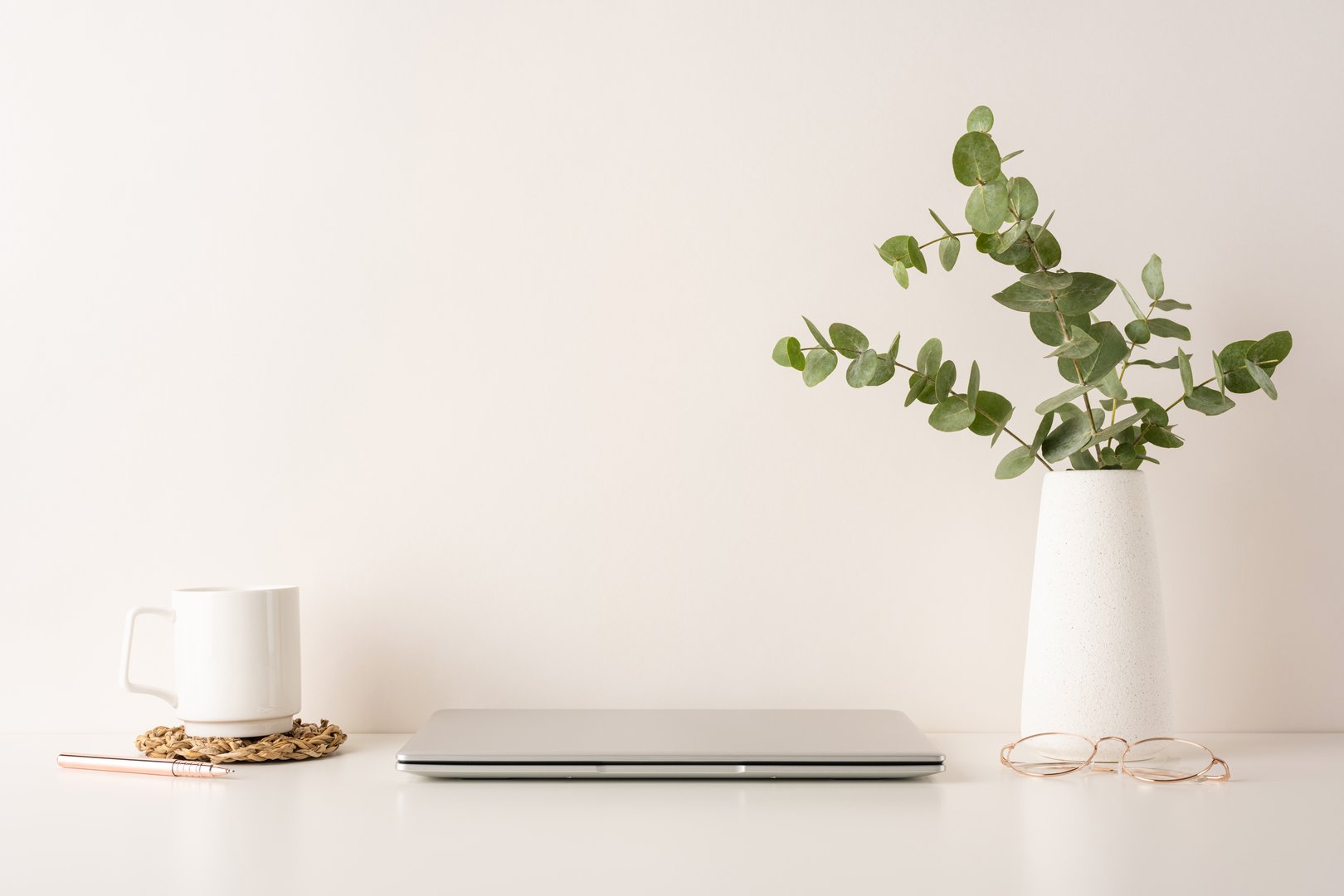 A neat and calming workspace setup featuring a laptop, coffee mug, pen, and pottery vase with eucalyptus. Perfect for minimal aesthetic enthusiasts and remote work productivity