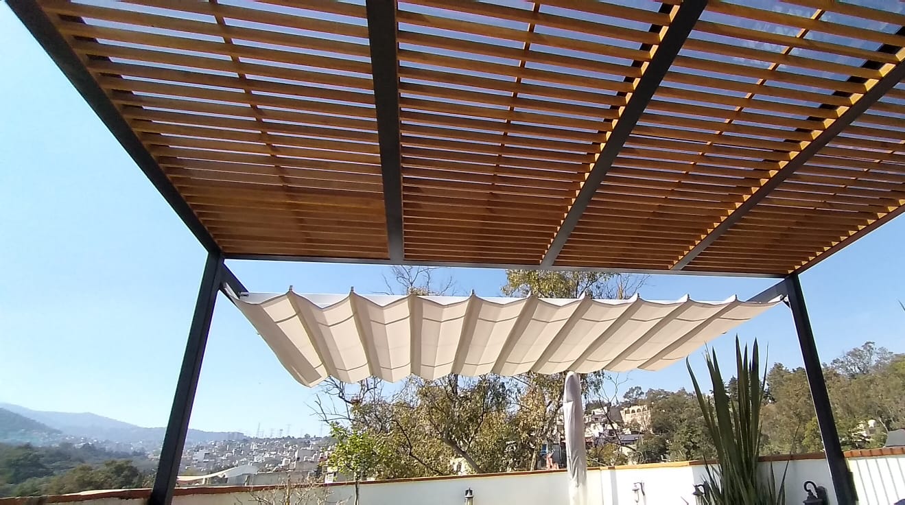 A patio with a wooden slat pergola and a retractable white canopy, overlooking trees and a distant cityscape.