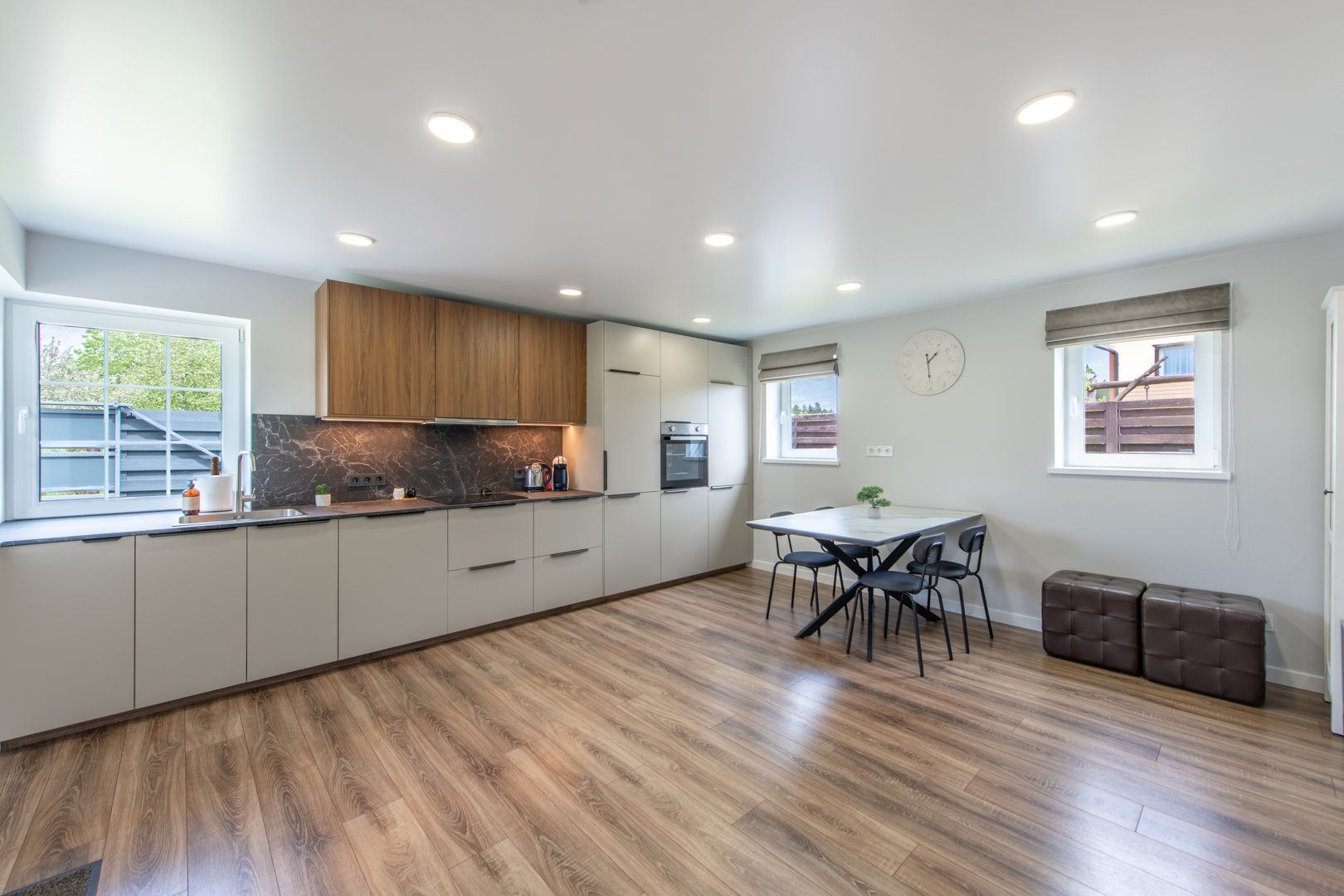 Spacious and well-lit modern kitchen with wooden cabinetry, a dining area, and sleek appliances. Elegant marble backsplash and laminated flooring complement the minimalist design