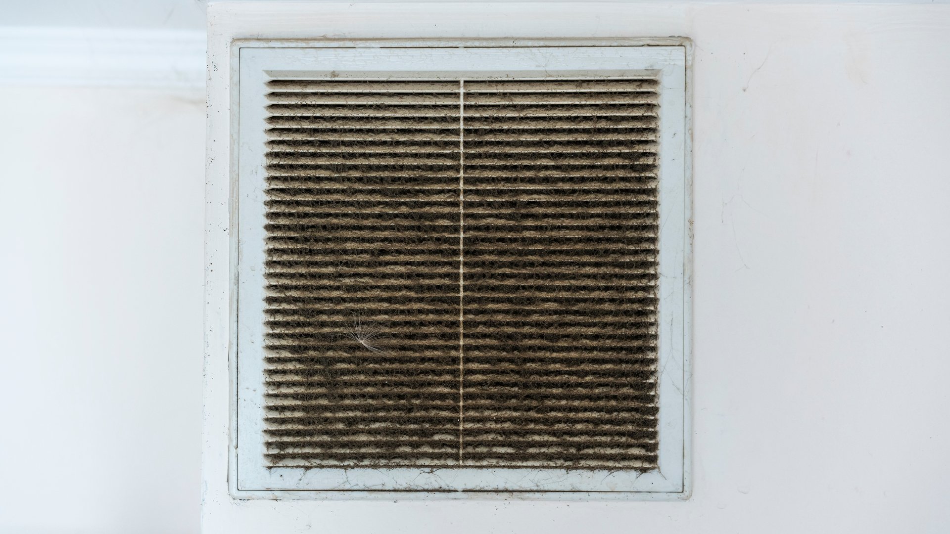 Dirty dust covered air vent is mounted on white wall showing accumulation of debris and neglect over time. Image highlights need for maintenance and cleaning in household ventilation system.