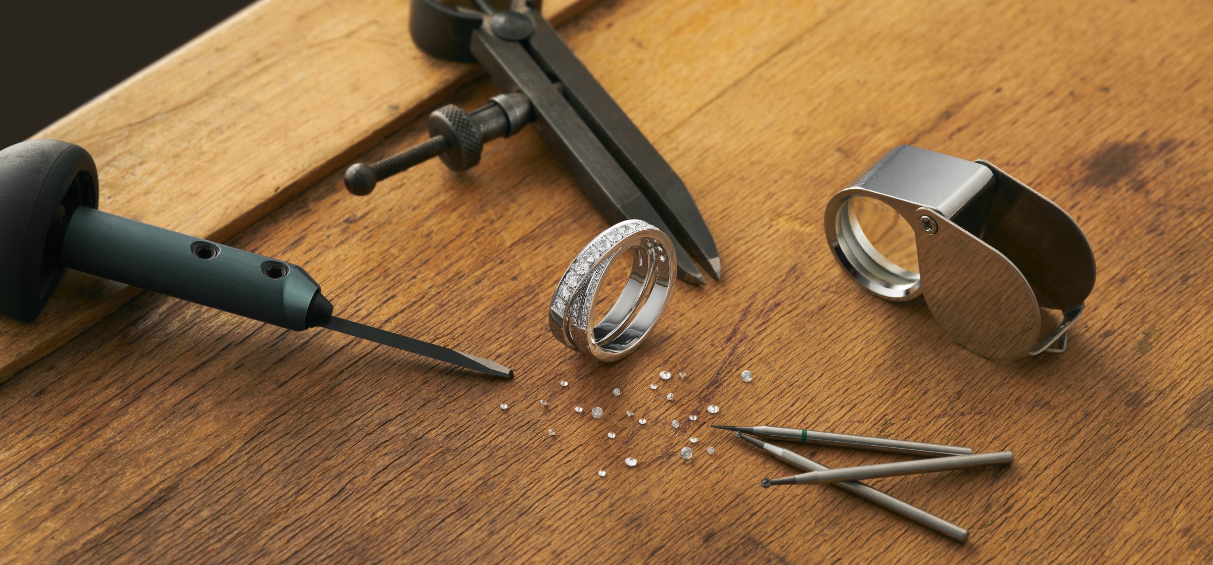 Workplace of a jeweler. Tools and equipment for jewelry work on an antique wooden desktop. Jeweller, engraver at work on jewelry made of diamonds and gold. Wood Platinum Diamond Metal Wide Background