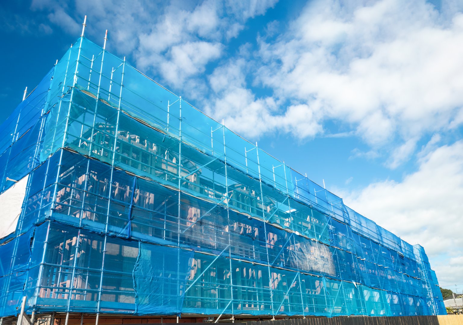 Residential house under construction. Blue sheet wrapping around the scaffolding. Auckland.