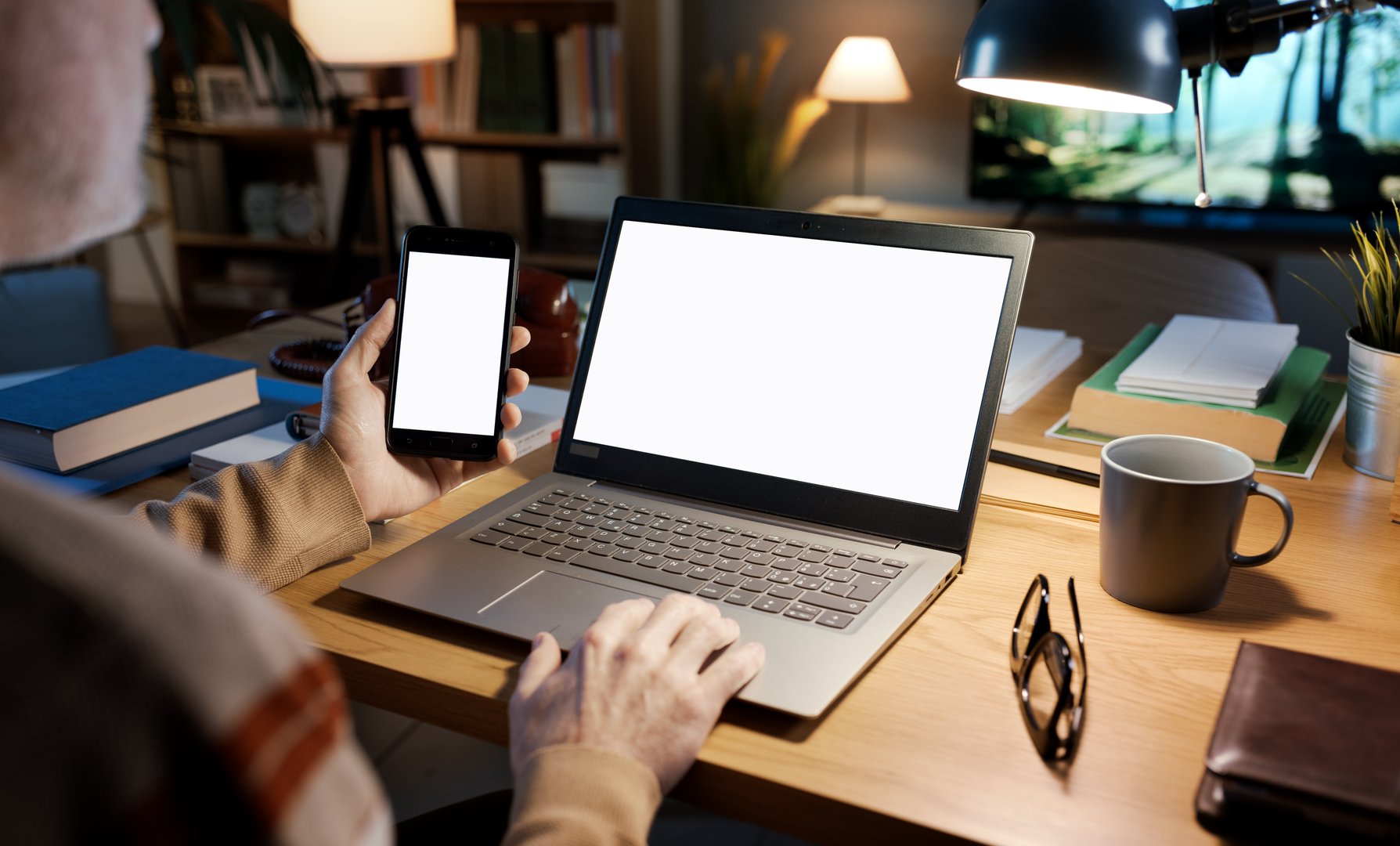 Man sitting at his desk and connecting to the internet using a smartphone and a laptop, the devices have blank screen