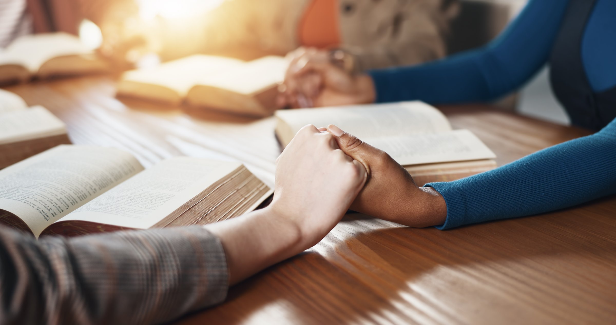 Hand holding, Bible and people with prayer for religion, guidance or support with scripture for worship. Christianity, faith and group by table, book of God and praise with spiritual education
