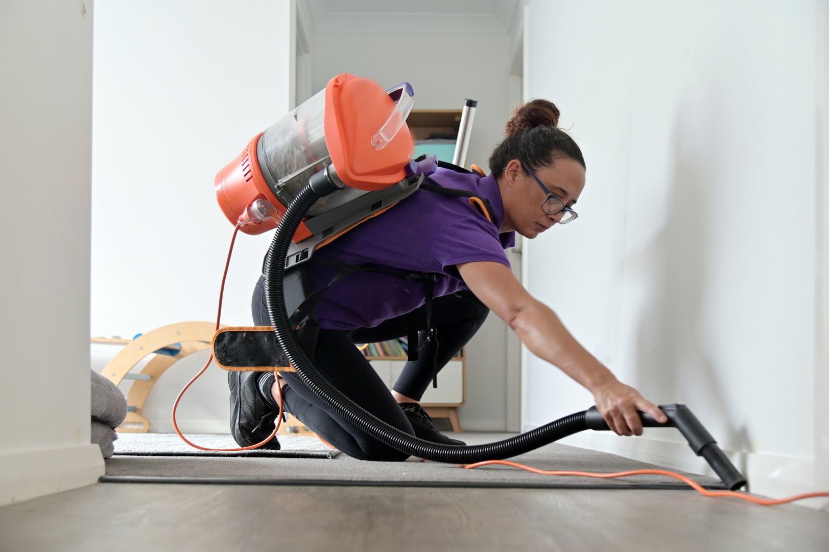 Professional house cleaner (female age 35-45) using a vacuum cleaner vacuuming dust from floor carpet.