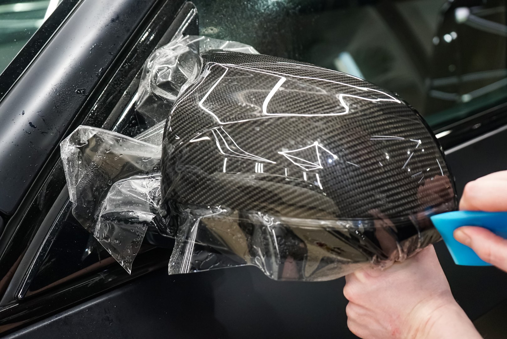 The process of installing PPF on the side mirror. Car wrapping close-up. Car wrapping. A car wrapping specialist applies a polyurethane film to the car. Selective focus. PPF protective film.