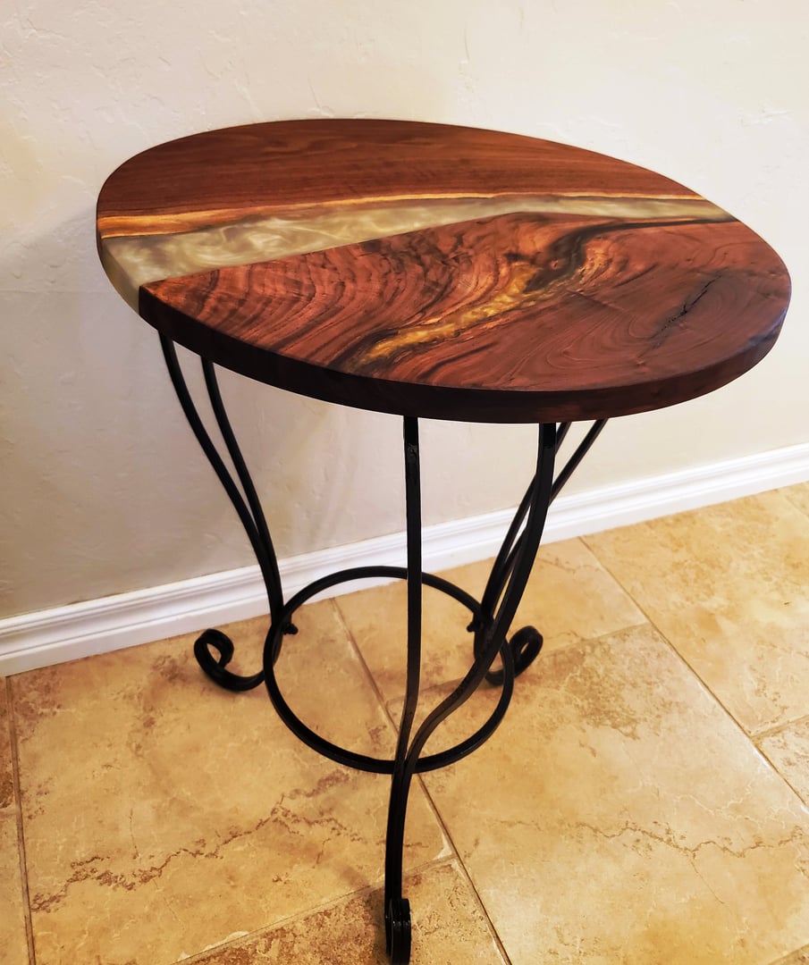 Round wooden side table with a resin river and black metal legs, on a beige tile floor against a white wall.