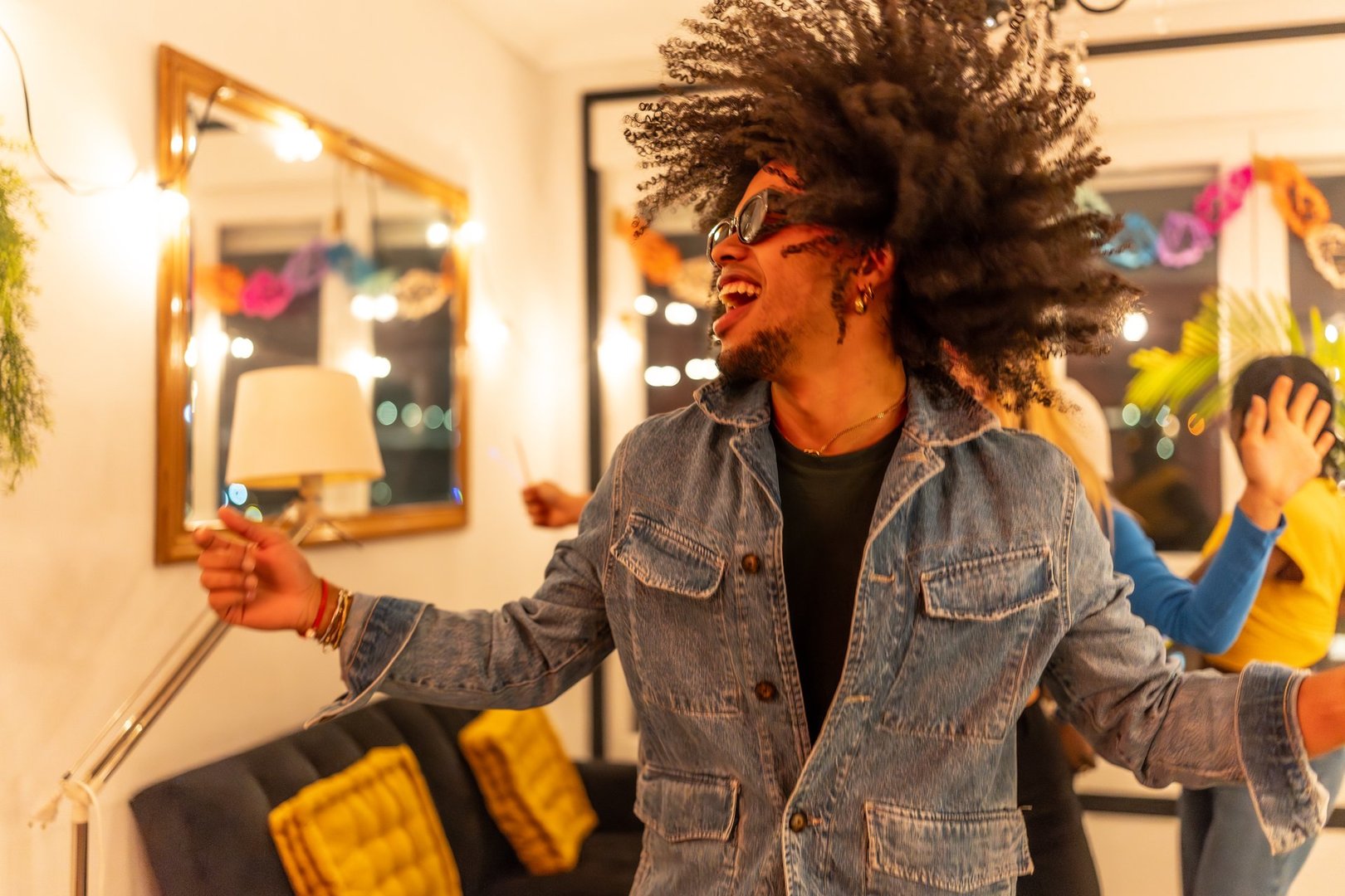 Young man with a large afro hairstyle dancing joyfully at home with friends, enjoying a lively house party filled with laughter and music