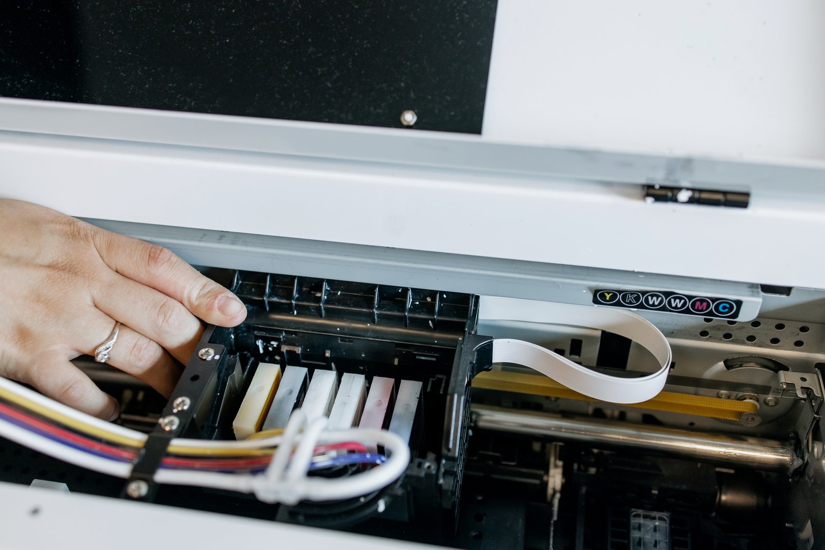 Close-up view of a professional inkjet printer during maintenance process, showing ink cartridges, printhead and ribbon cable inside industrial printing equipment