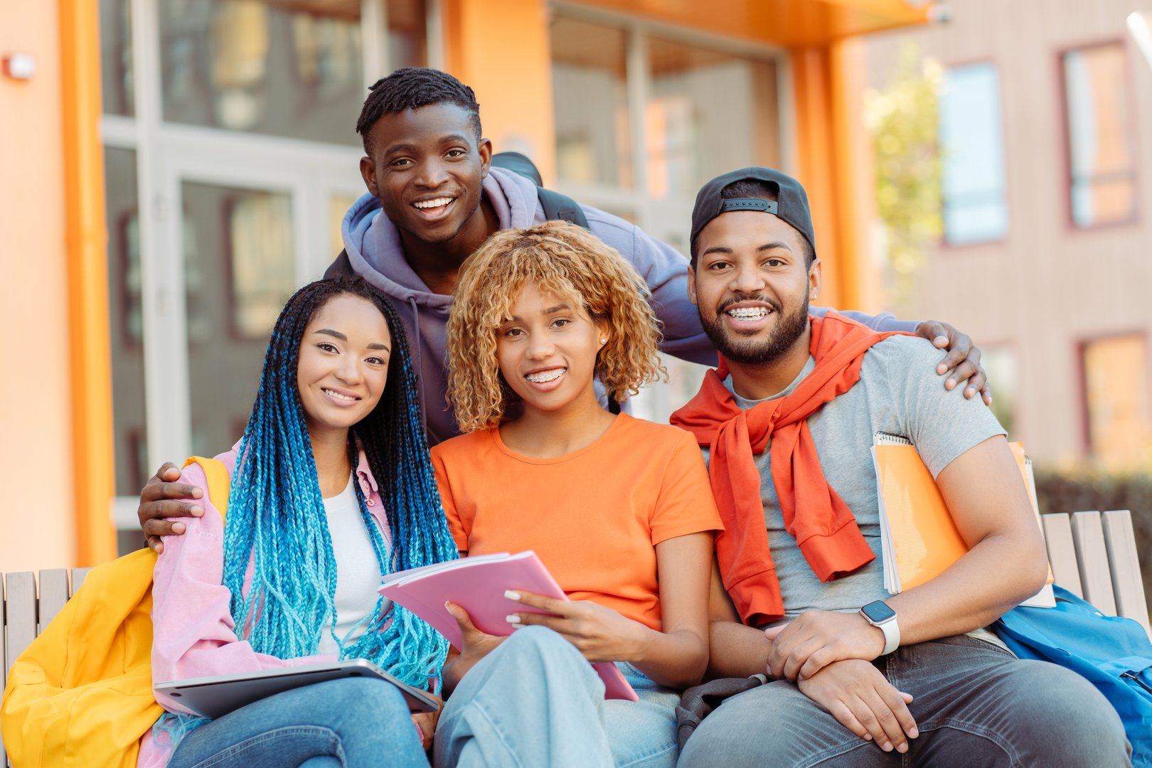 Smiling diverse African American friends in colorful casual clothes looking at camera near university campus on street. Happy students outdoors. Concept of education, communication, meeting