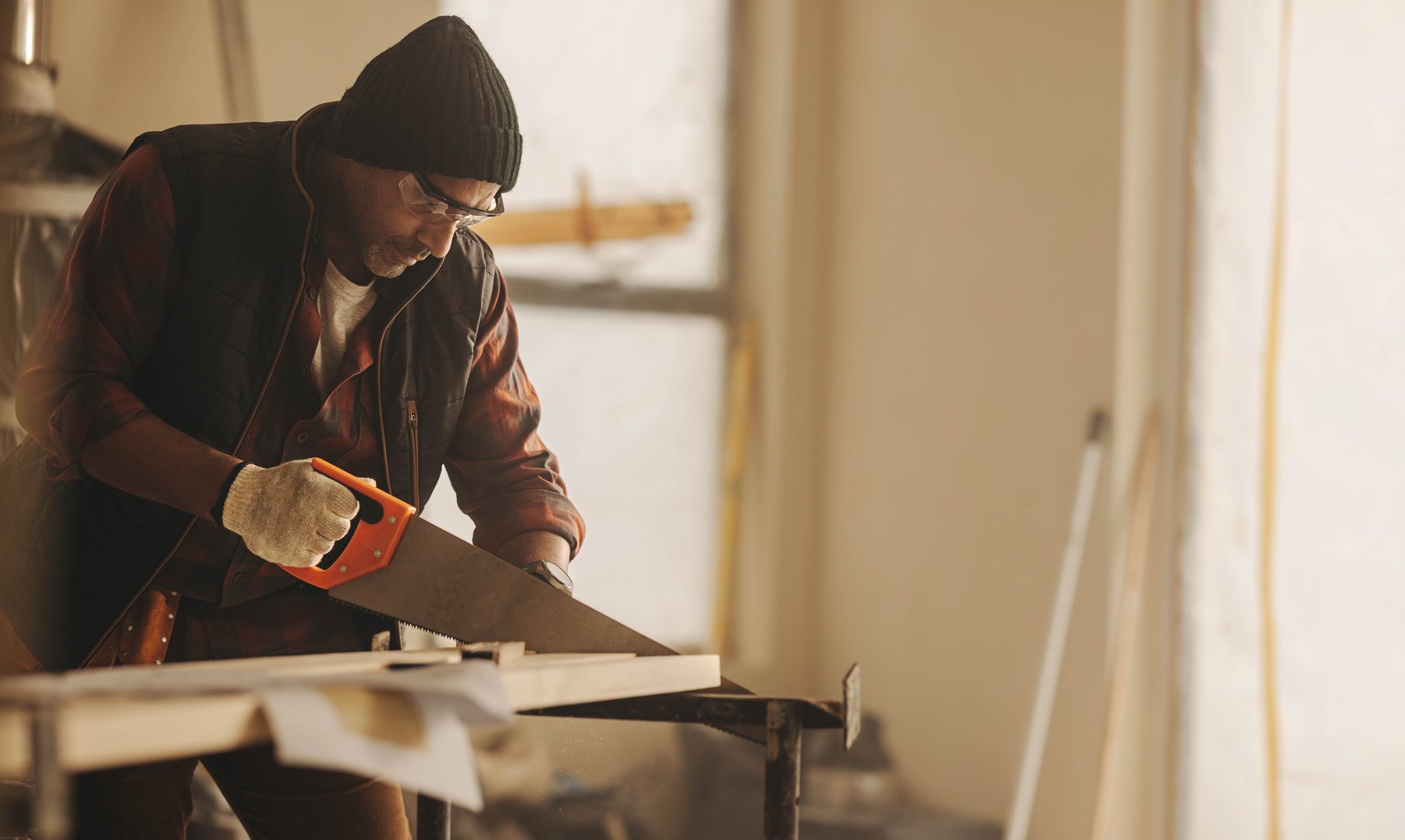 Building contractor renovating a kitchen, using a saw to cut wood. He is focused on the home improvement project, undertaking remodeling and refurbishment work with precision.