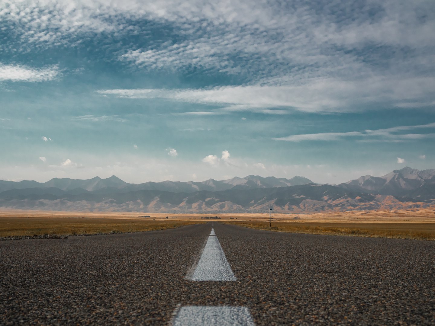 Endless highway stretching to horizon through steppe with distant mountains, symmetrical composition