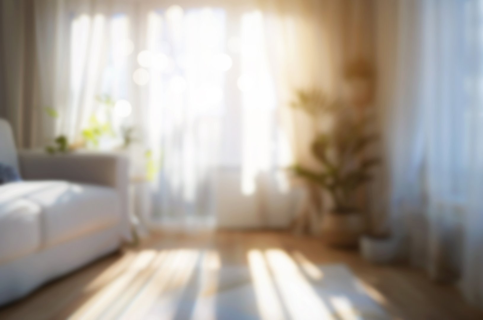 Blur interior design background illuminated by sunlight, with sofa and large window.