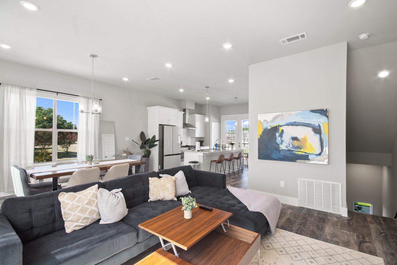 Modern living room with a black sofa, wooden coffee table, kitchen in the background, and abstract art on the wall.