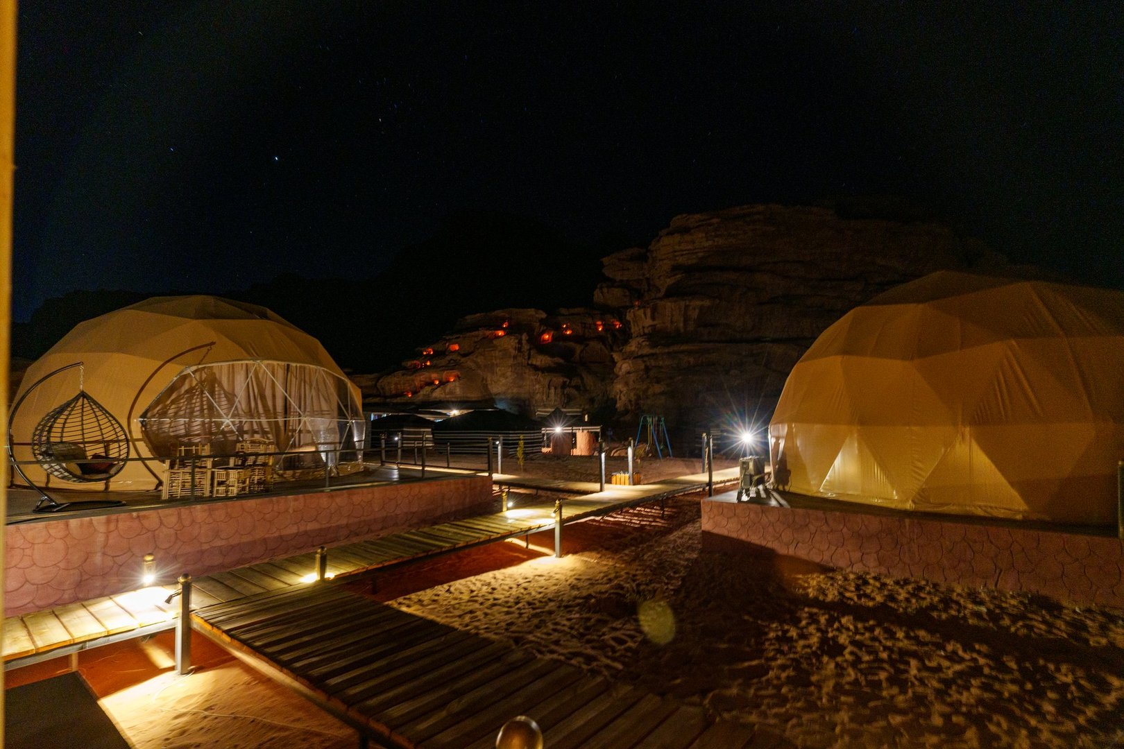 Illuminated domes under a star-lit desert sky create a serene and adventurous nighttime camping atmosphere with cozy accommodations.