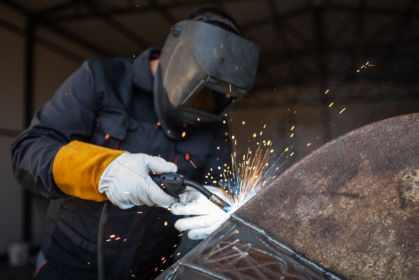 Metal worker is welding a steel structure in a workshop, creating a shower of bright sparks