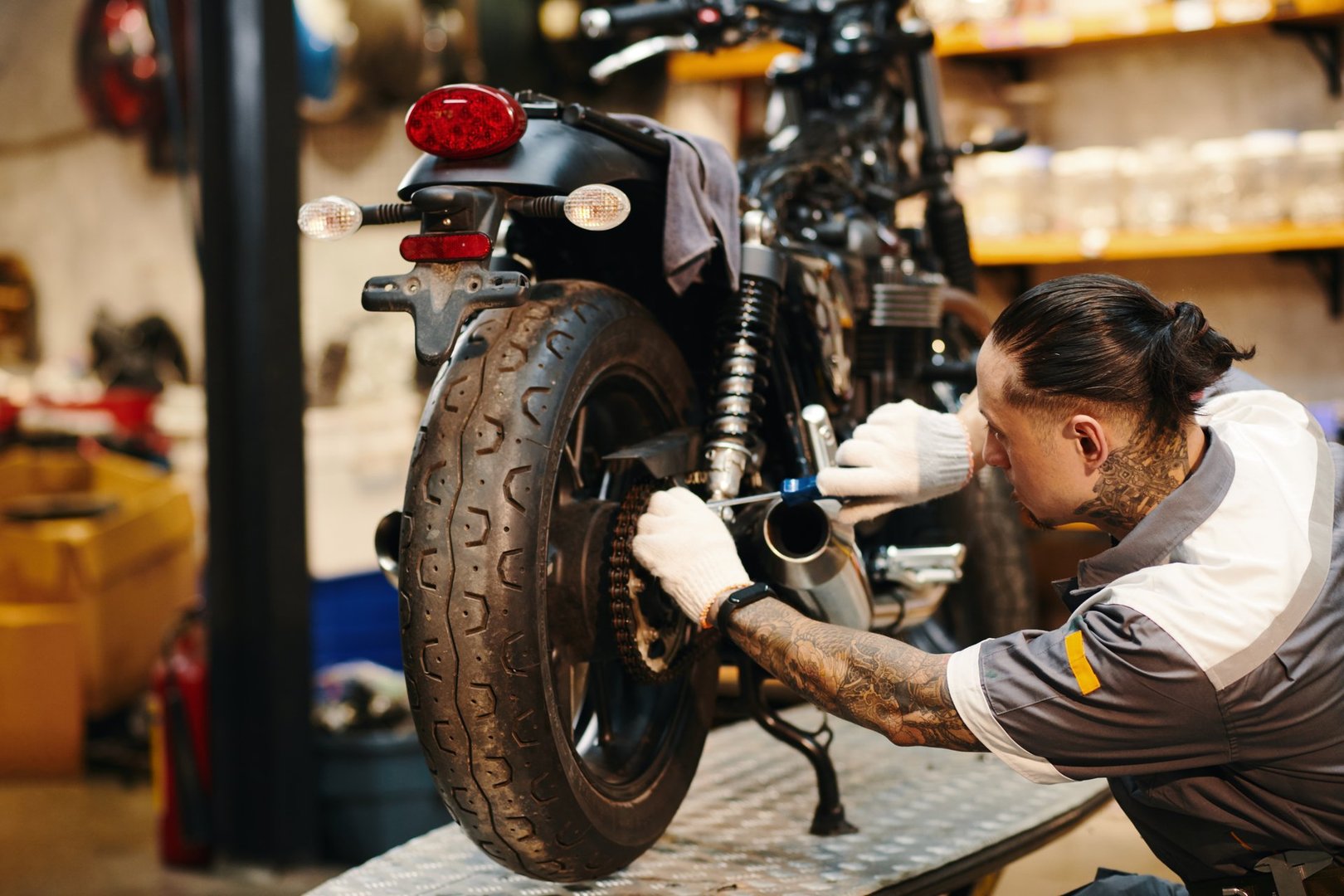 Mechanic in uniform and textile gloves fixing chain of motorcycle