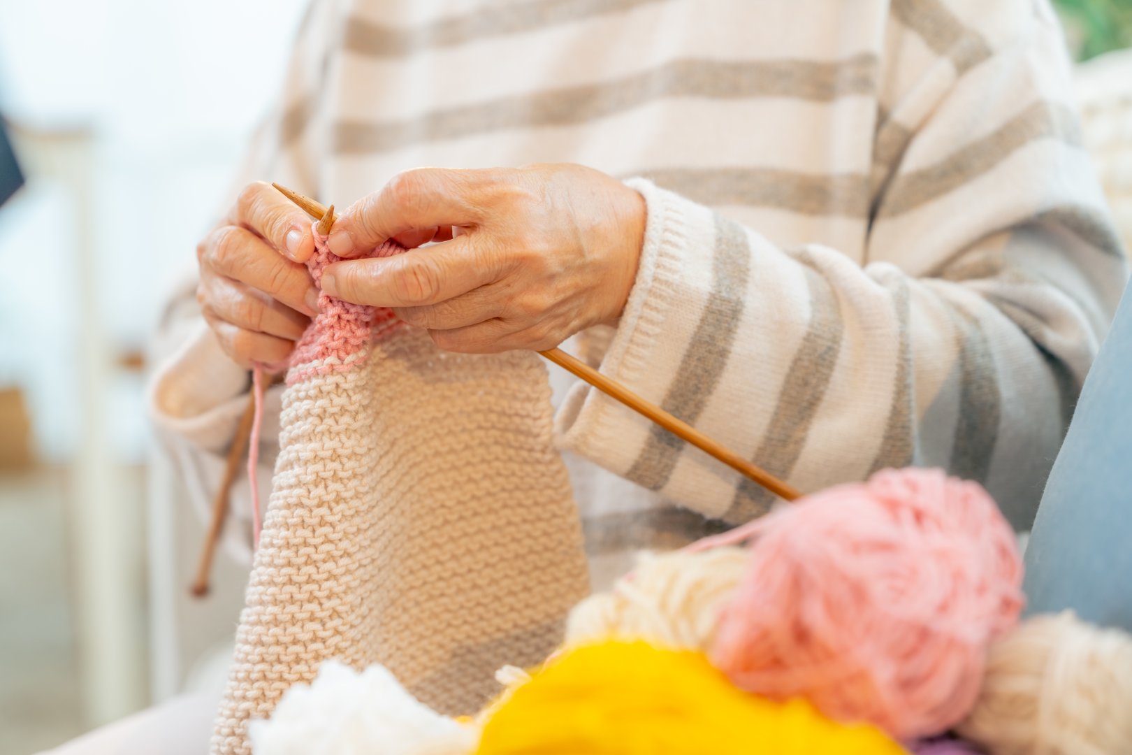 Happy Asian elderly woman grandmother sitting on sofa knitting with needles and thread in living room. Retired old woman relax and enjoy indoor lifestyle leisure activity hand craft hobby at home.