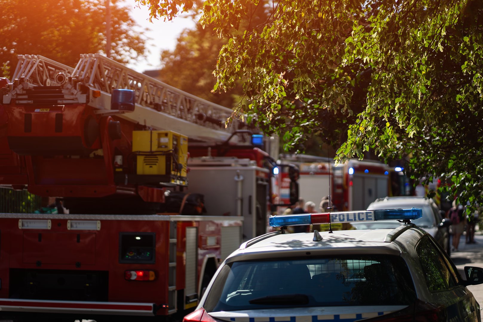Firefighters and police respond to emergency, fire trucks with ladders and flashing blue lights. Firemen in gear prepare equipment in residential area. High quality photo