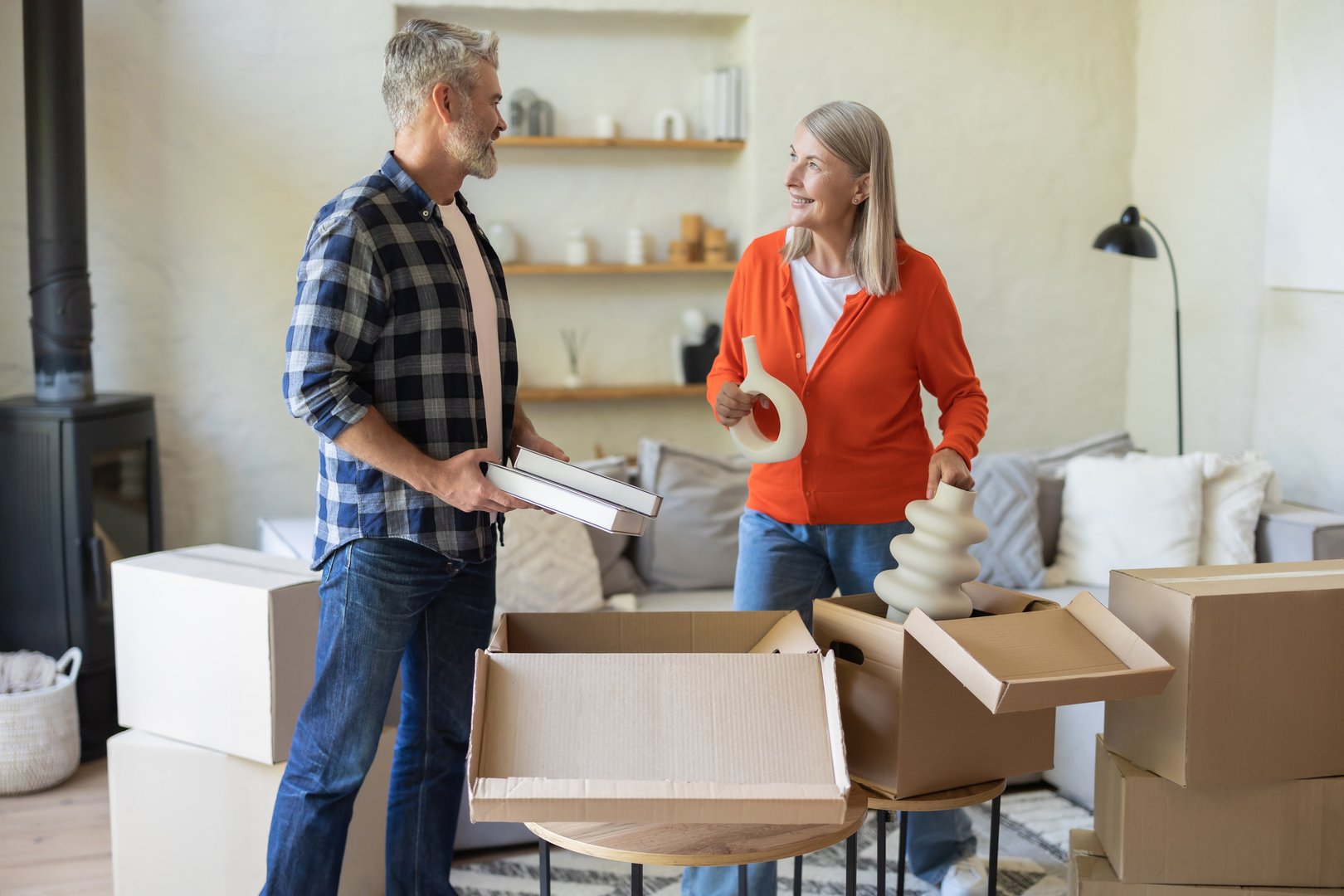 Happy senior couple standing indoors surrounded by unpacking boxes