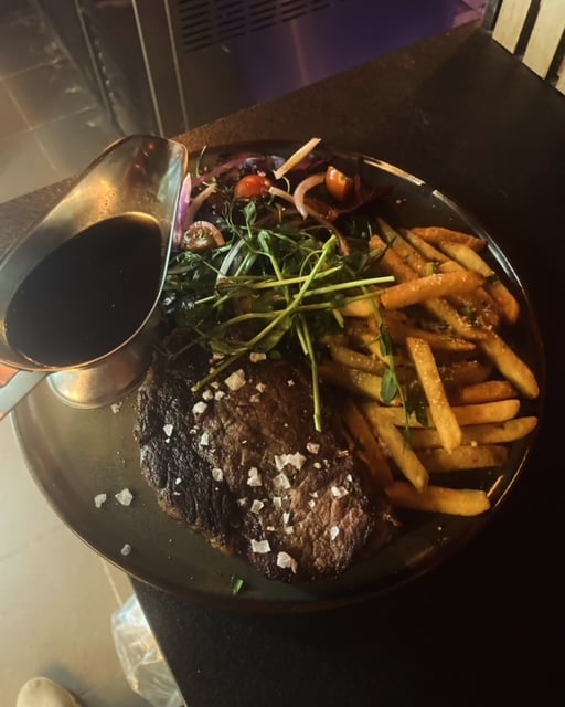 Grilled steak with sea salt, fries, salad, and sauce served on a dark plate.