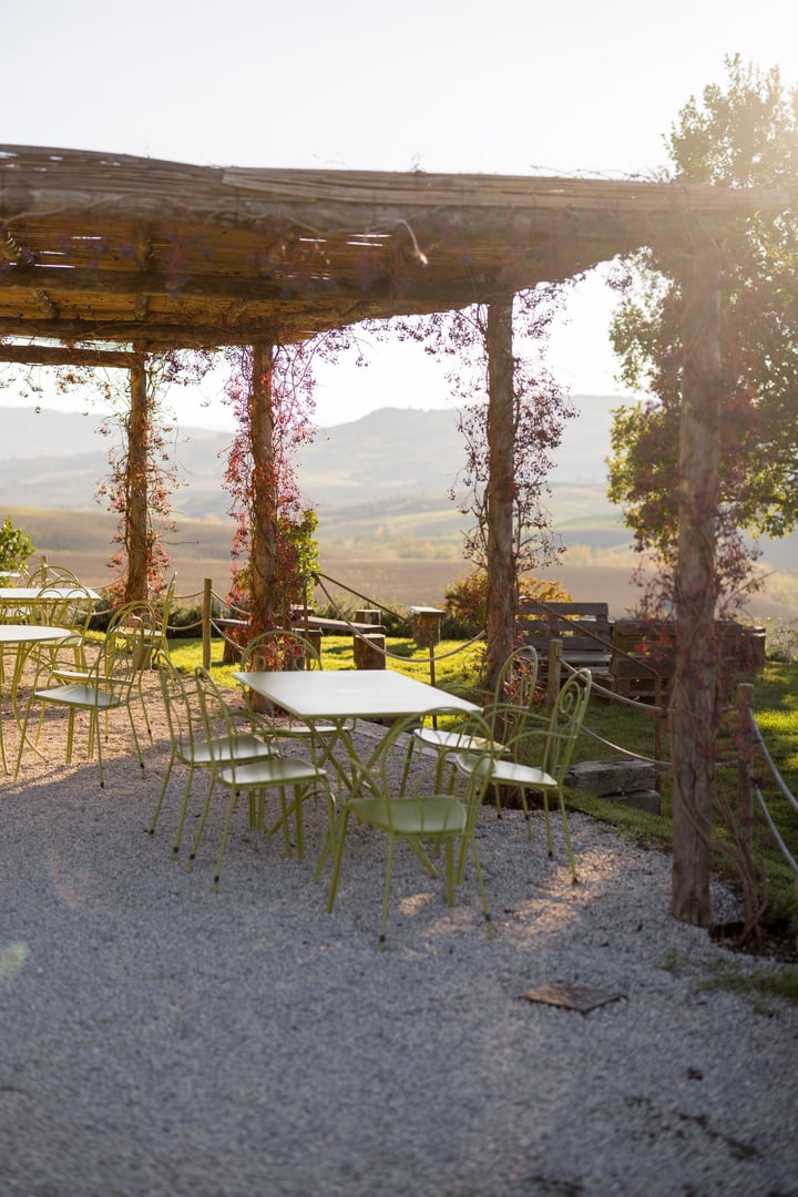 Rustic outdoor dining area under a vine-covered pergola with scenic views of the Tuscan countryside. Perfect for themes of relaxation, nature, and Mediterranean lifestyle