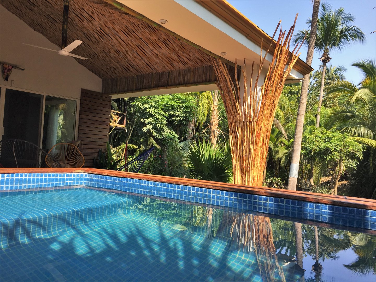 Tropical resort pool with a thatched roof structure and lush greenery in the background.