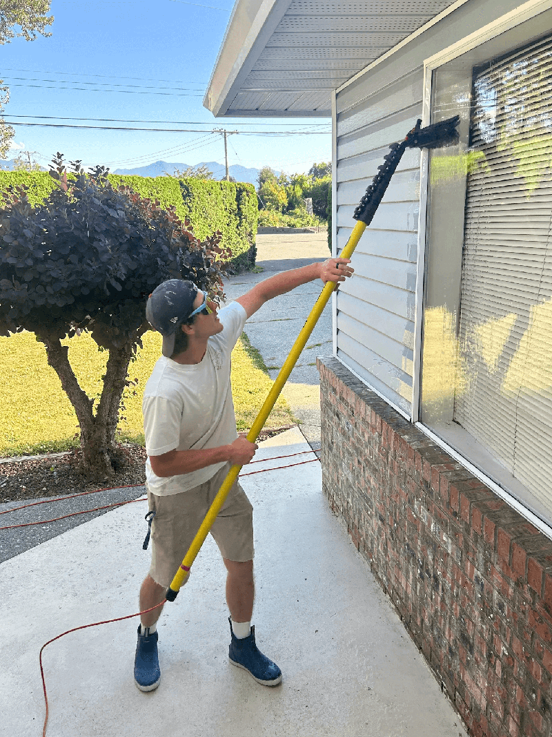 Worker in overalls washes a white wall from a siding with a water gun. Cleaning service for washing buildings and facades