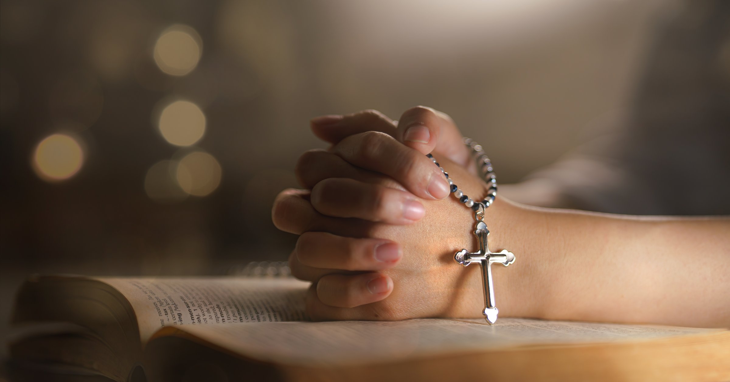 christian religion background with light bokeh christian woman hand on holy bible praying to god holding cross rosary selective focus at cross. concept of christian religious people faith and practise