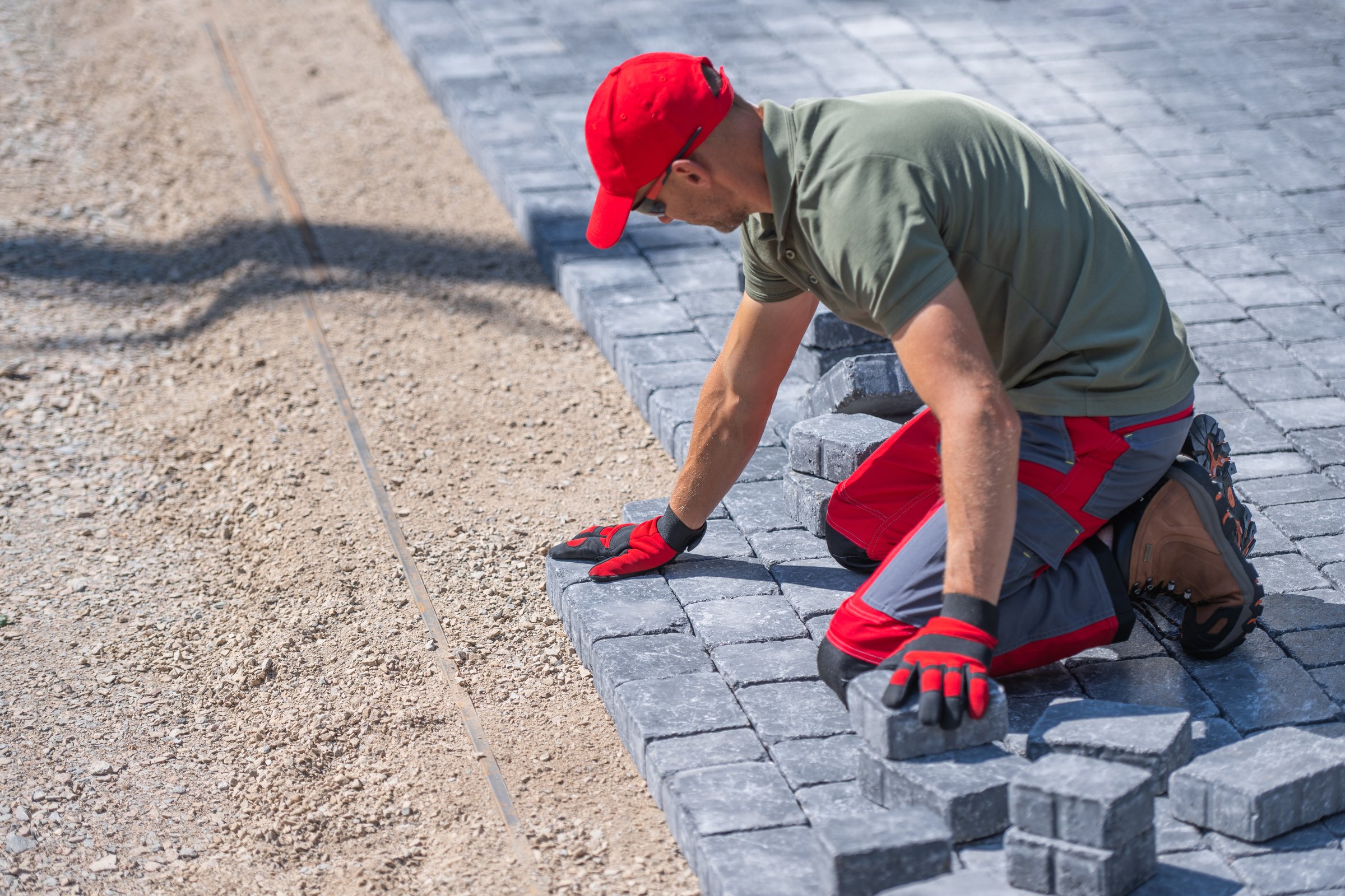 A worker is carefully laying down pavers on a prepared gravel base, focusing on alignment and precision.