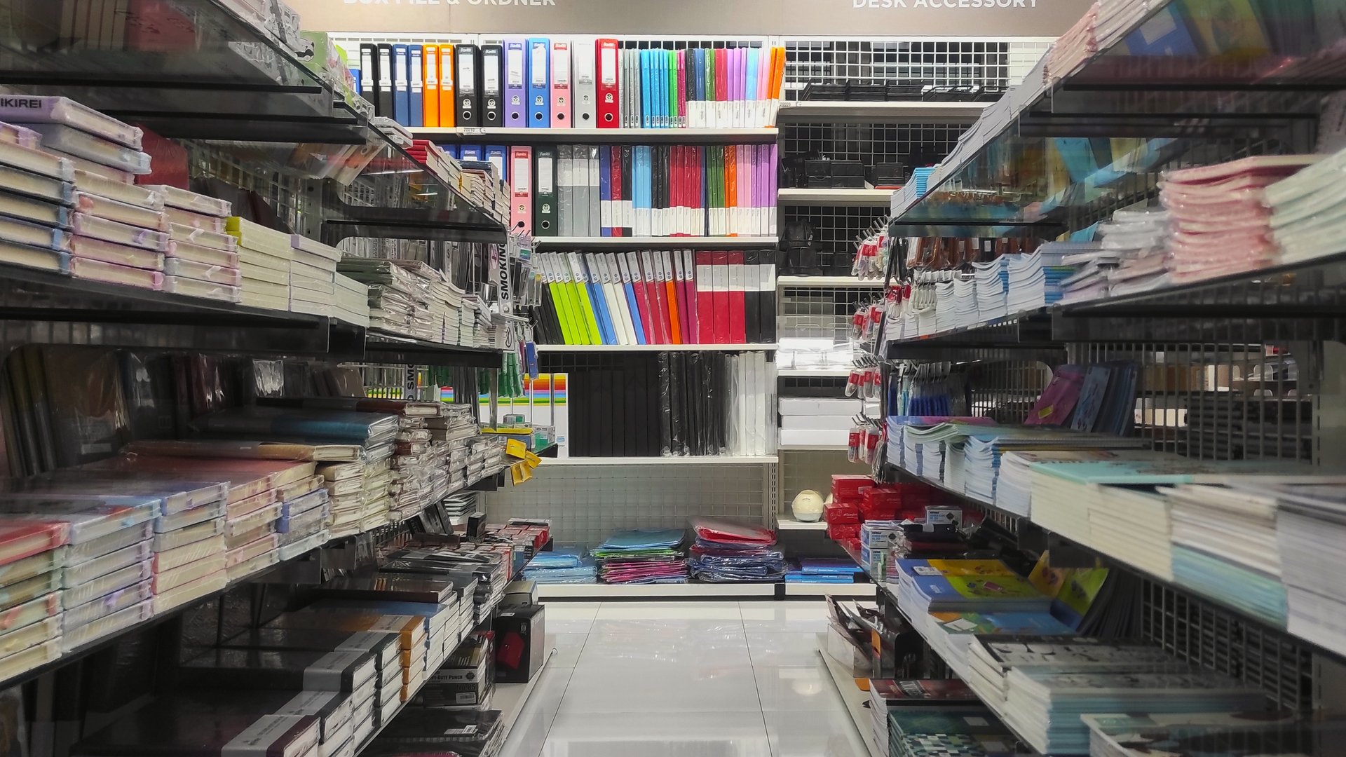 A neatly organized stationery aisle in a store, filled with notebooks, binders, and office supplies on both sides. The shelves display various colorful items, creating a sense of order and variety