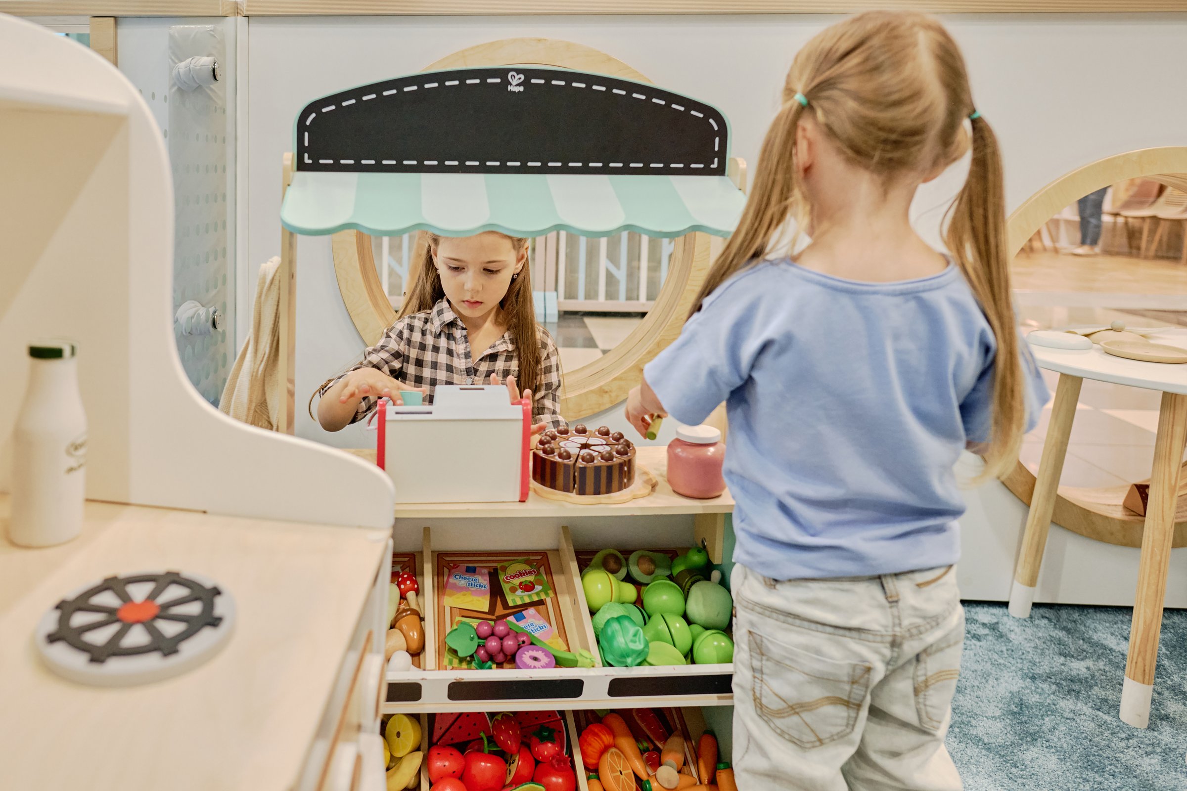 Rear view of little buyer with ponytails standing in front of market stand with clerk holding drink while serving friend