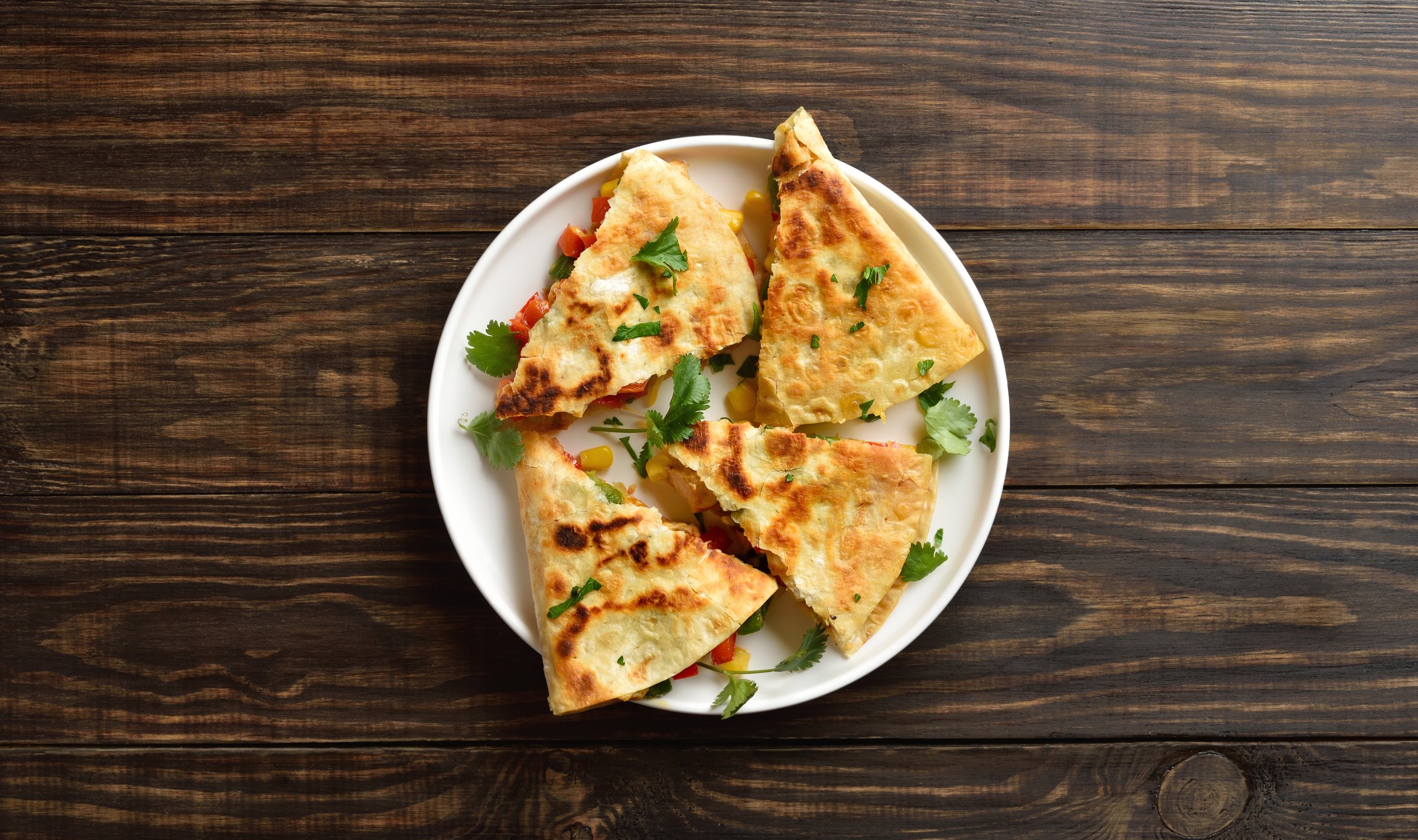 Chicken quesadillas with fresh vegetables on white plate on brown wooden background. Top view, flat lay