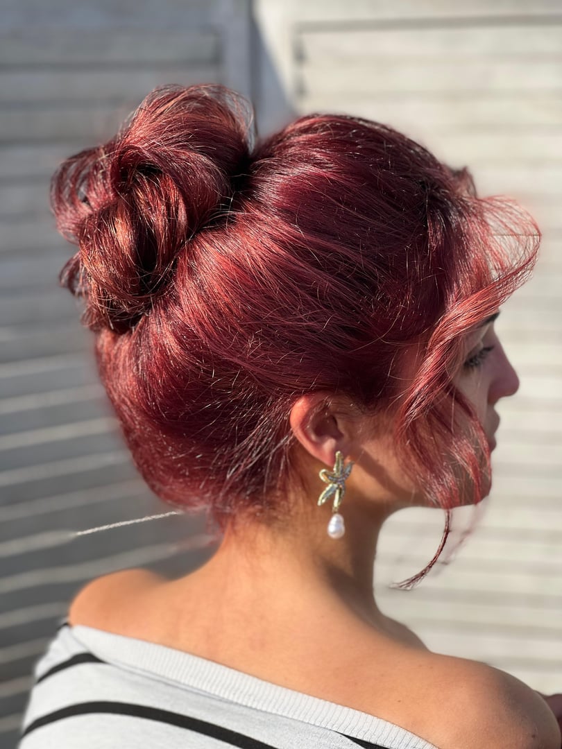 Woman with red hair in an updo and a pearl earring, wearing a striped top, facing a wooden background.