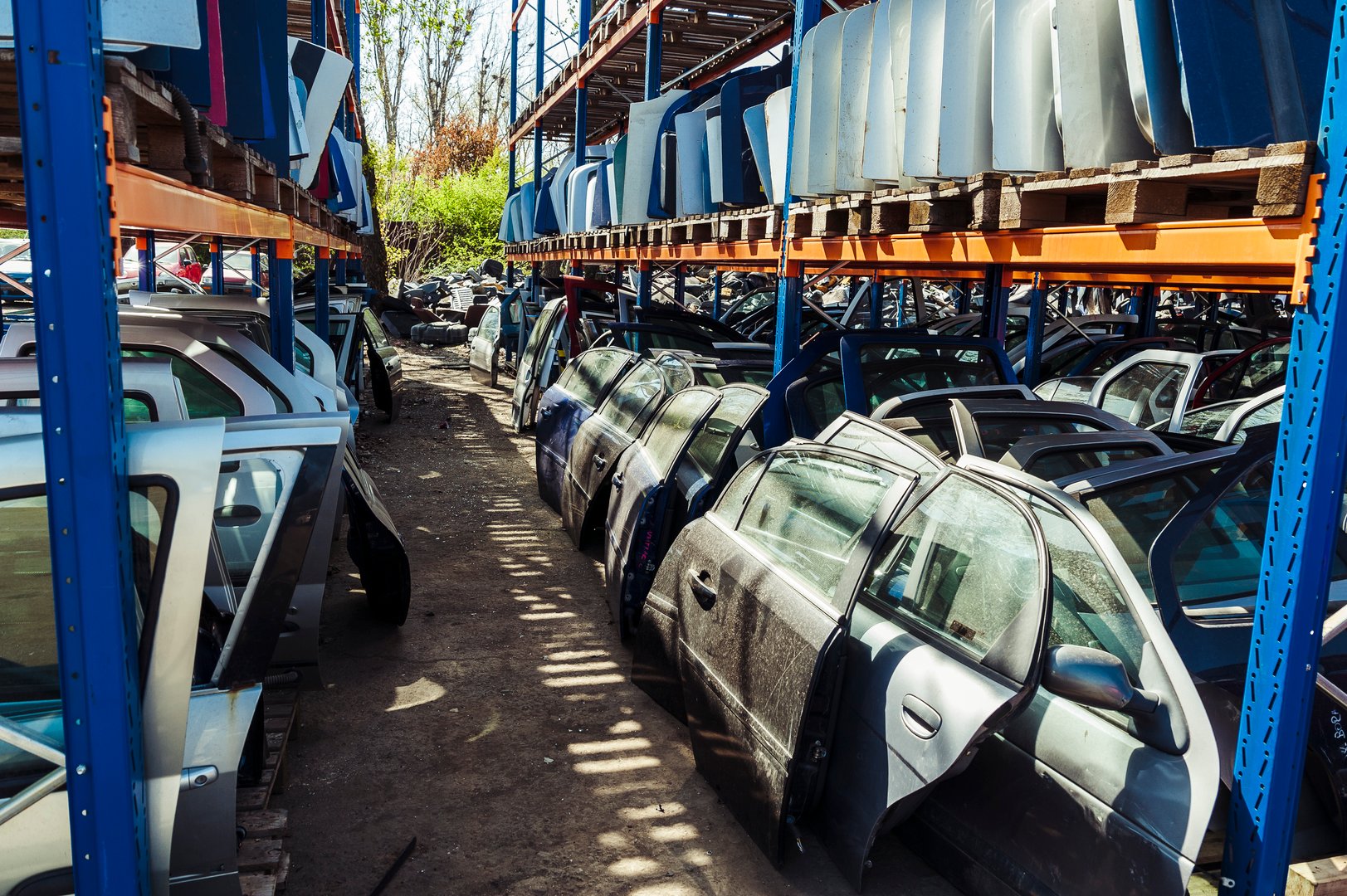 Car doors and windows sitting in layered rows in a recycling center after being disassembled.
