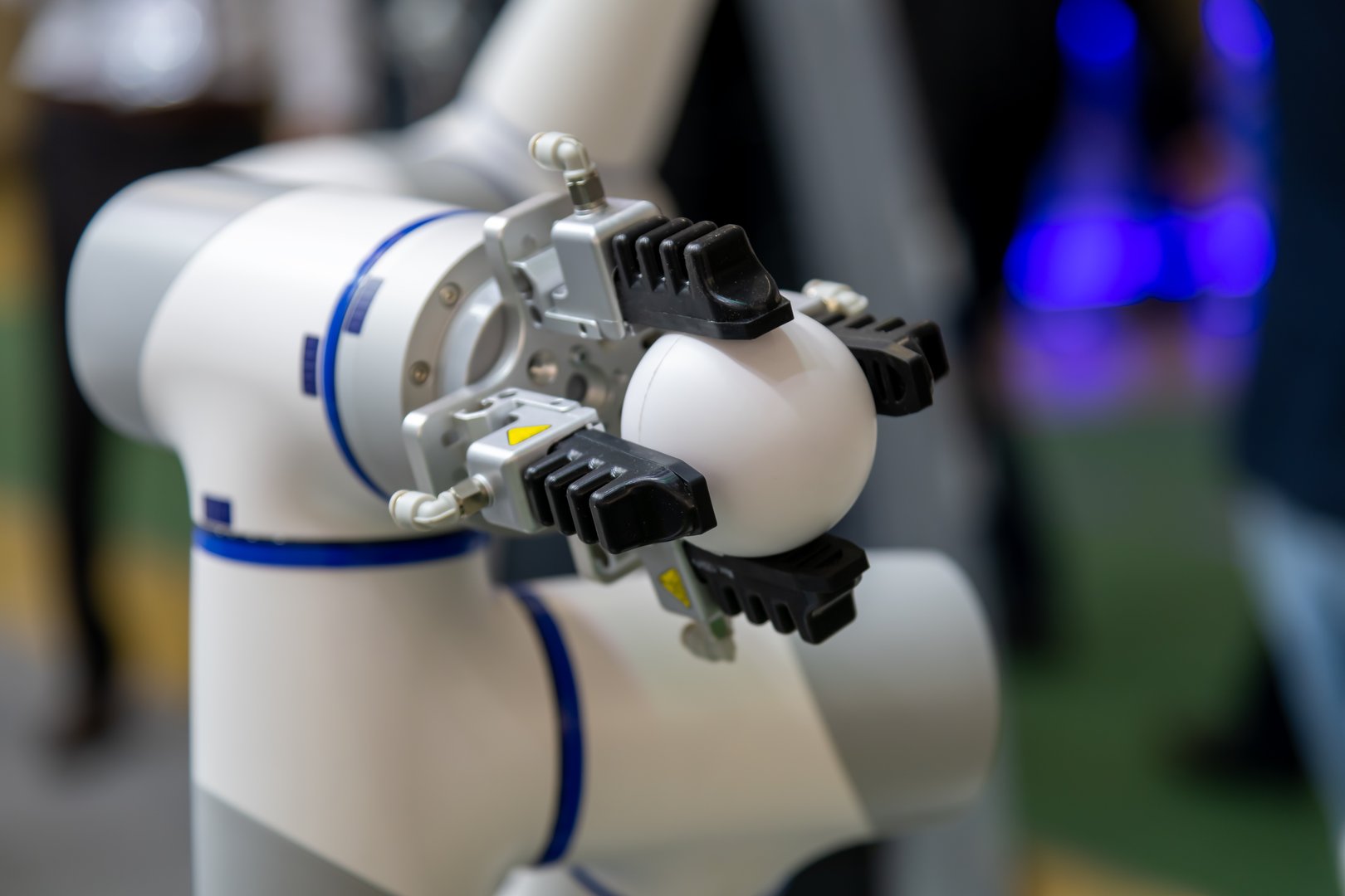Close-up view of modern white and grey robotic arm manipulator holding white ball in industrial building. Soft focus. Copy space. Industrial high technology theme.