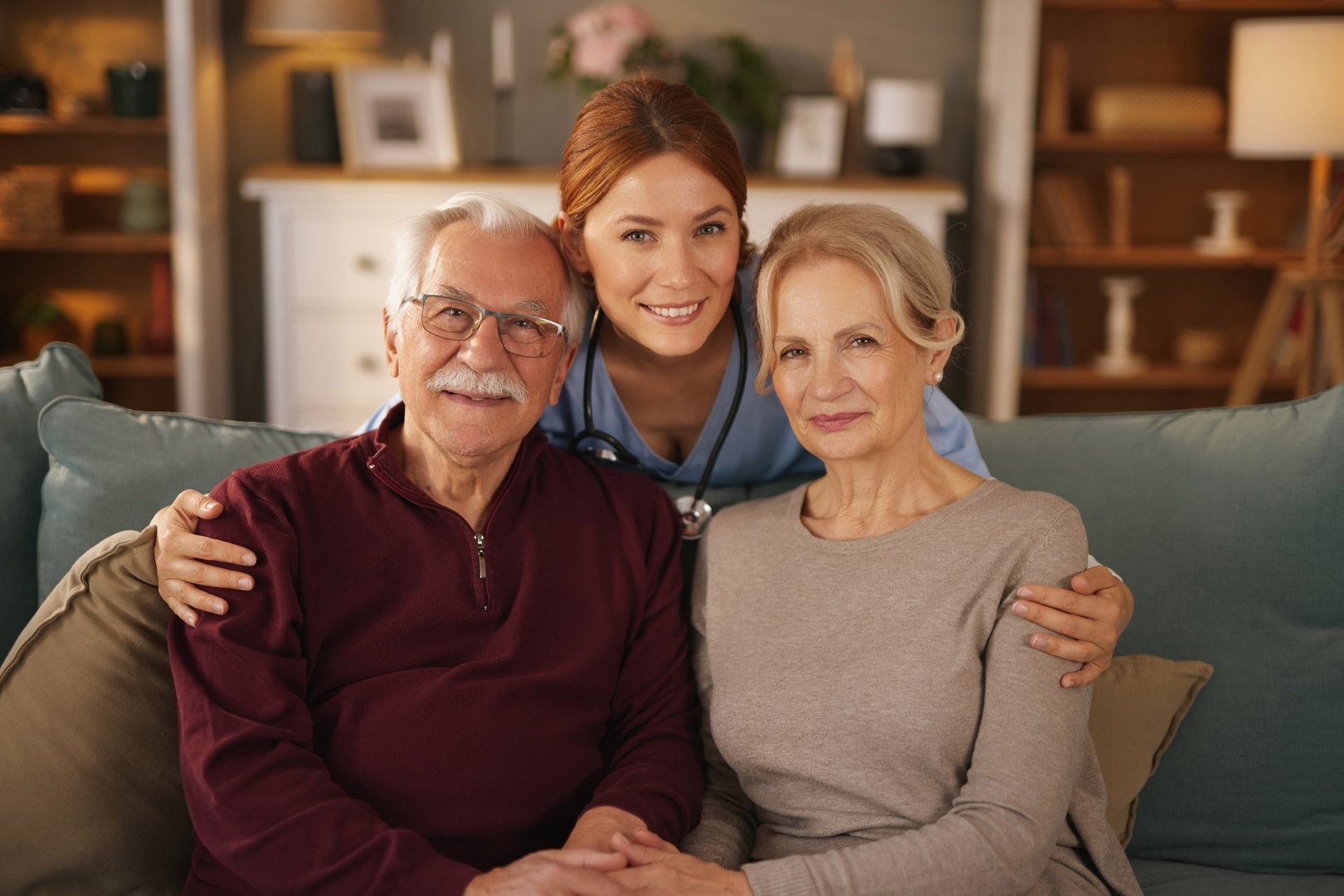 Cheerful home nurse embraces a happy senior couple on a comfortable sofa, showcasing the importance of healthcare and support for the elderly