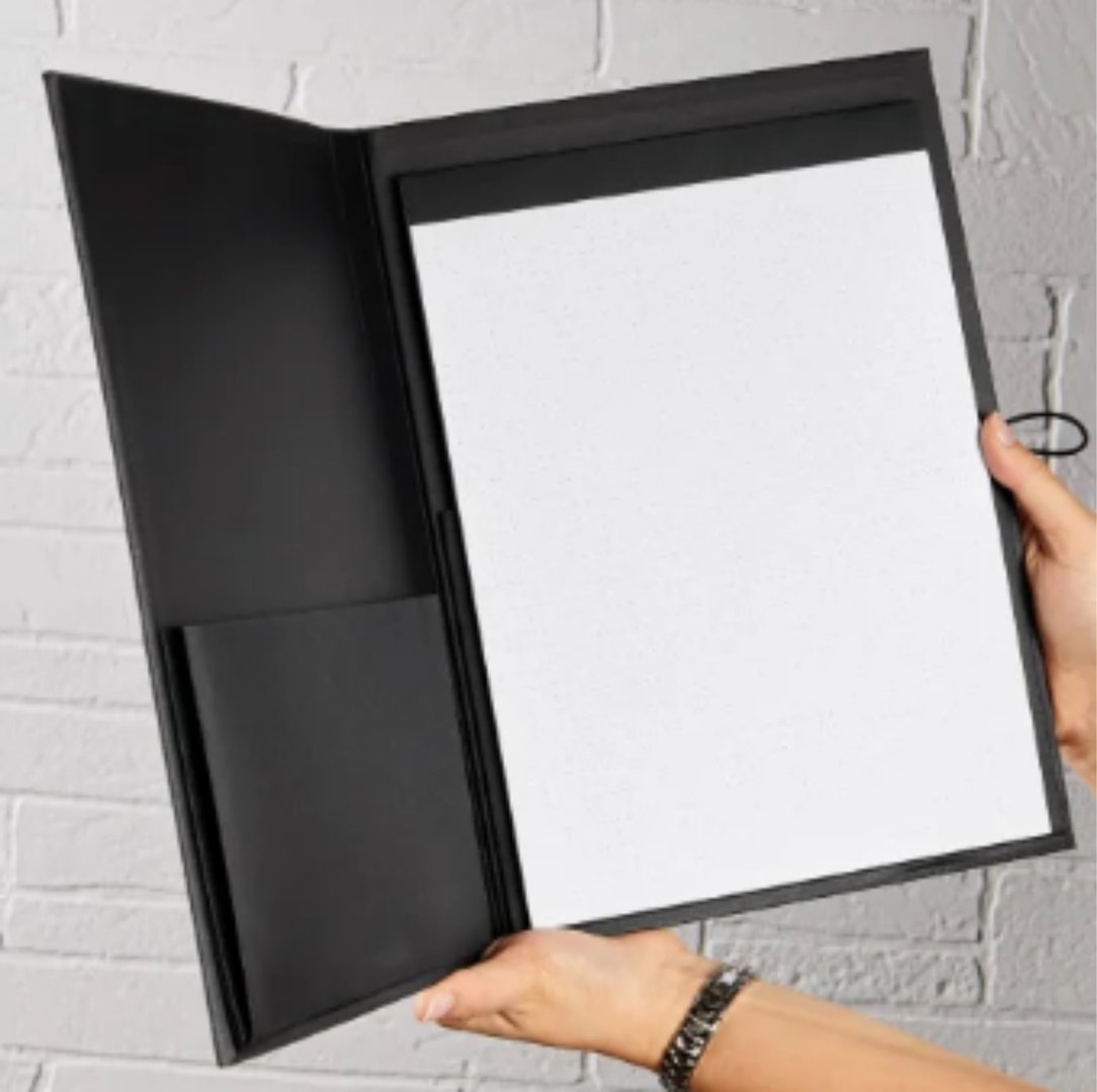 Hands holding an open black folder with a notepad inside against a white brick wall background.
