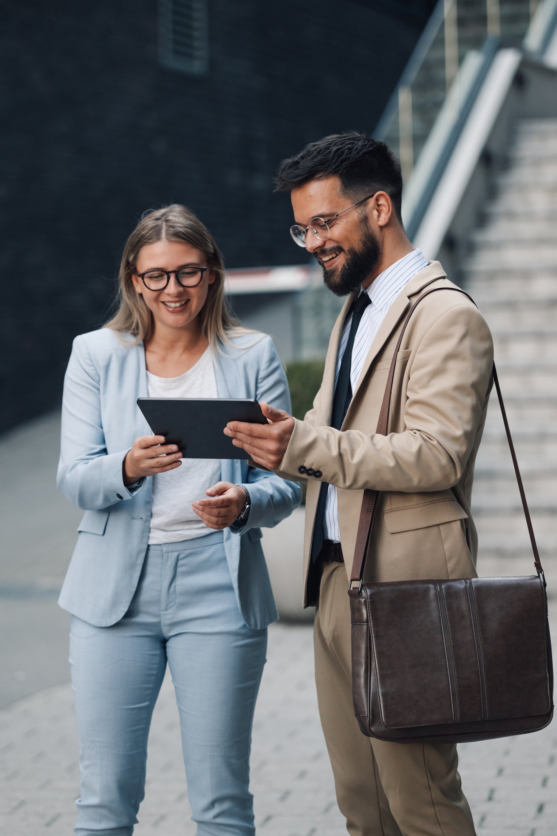 Two young business partners smiling and using a digital tablet outdoors, discussing a project with deep engagement and collaboration