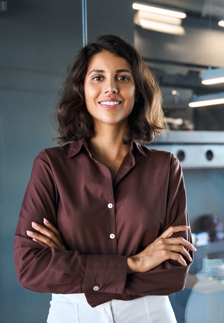 Vertical portrait of beautiful successful hispanic young business woman with crossed arms smiling confident at camera. Latin or eastern middle age female ceo leader businesswoman standing in office