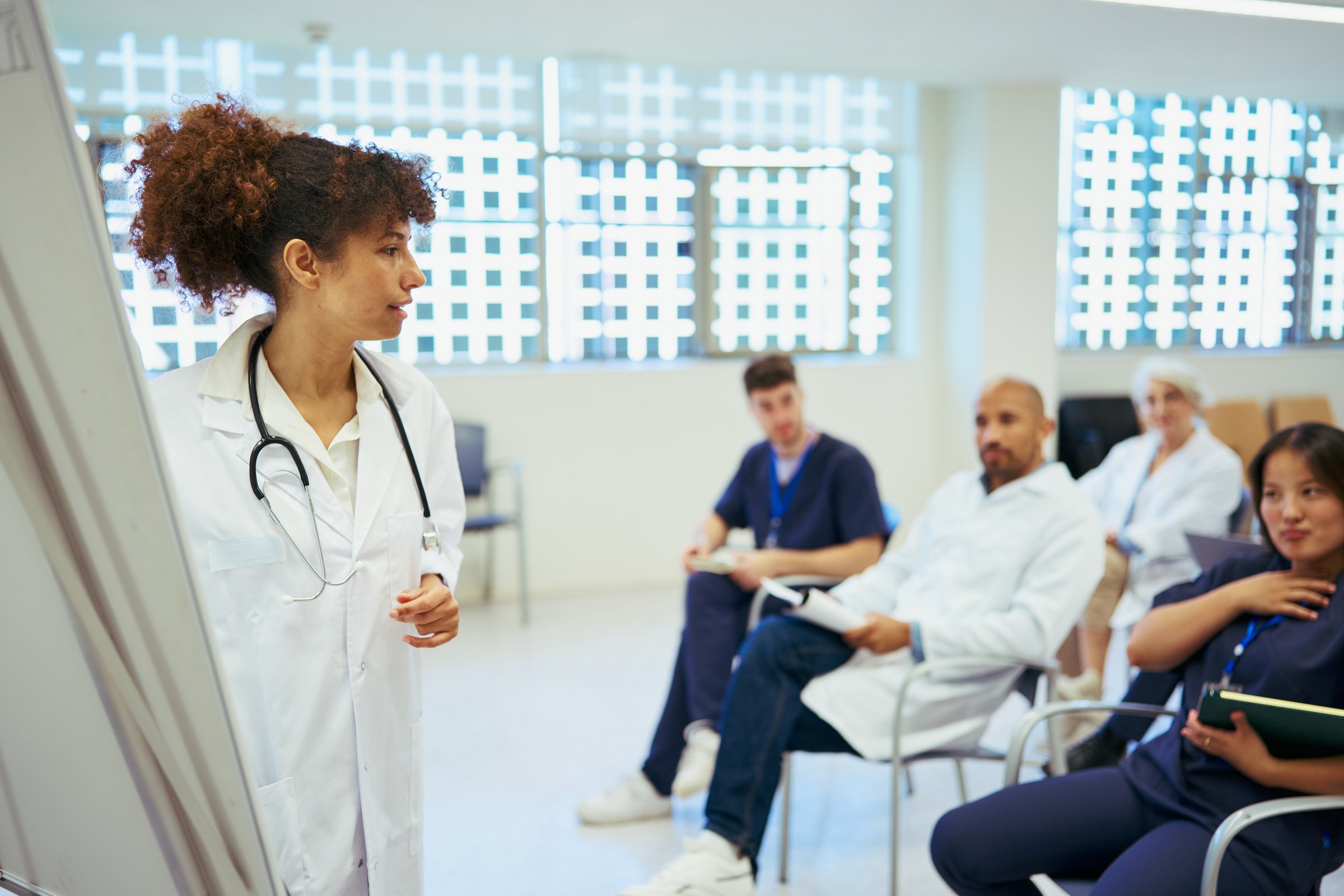 Diverse medical team attending a presentation held by a female doctor in a hospital setting, focusing on healthcare, training, and teamwork