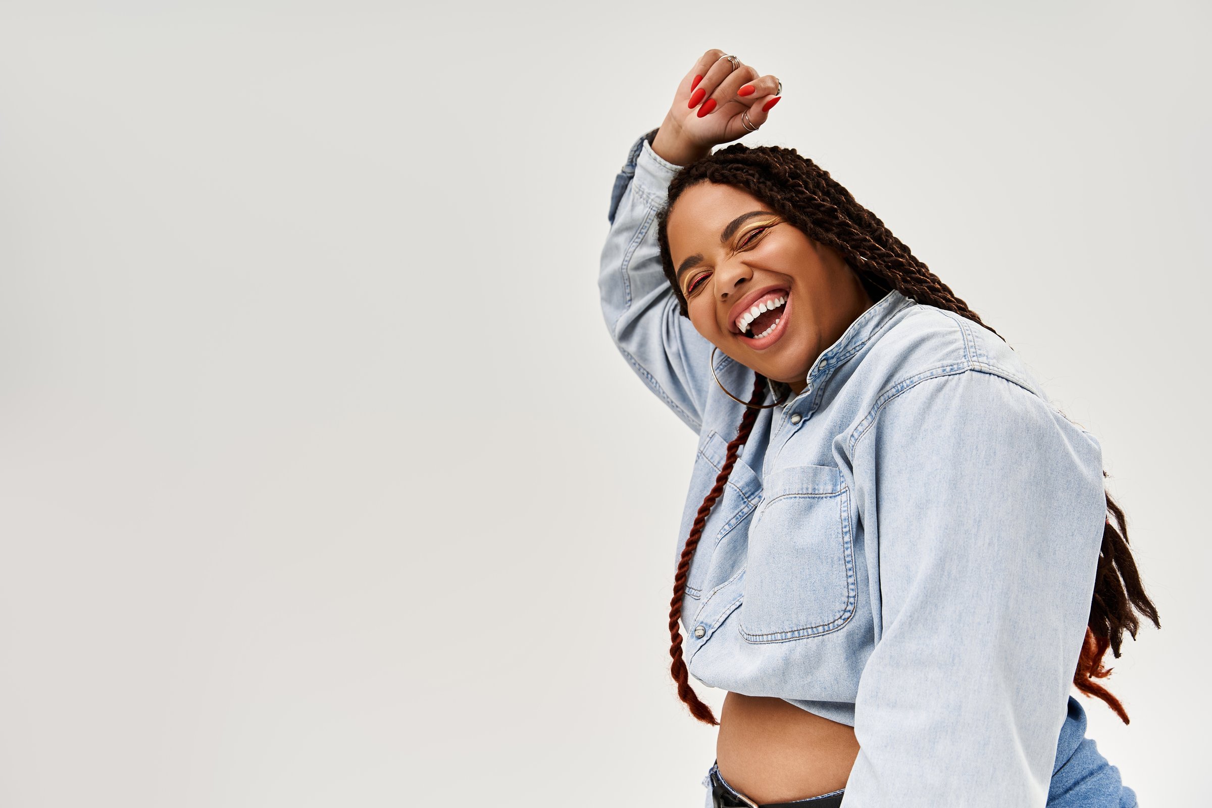 A vibrant African American woman with braids joyfully poses in denim, exuding confidence and bliss.