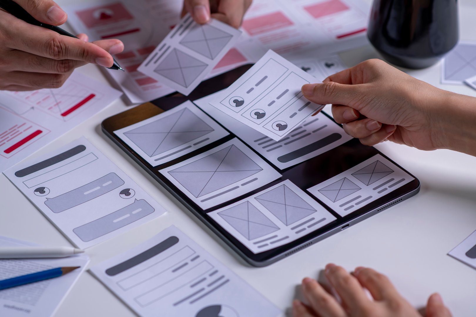 Close up UX developer and UI designer brainstorming about mobile app interface wireframe design on table.