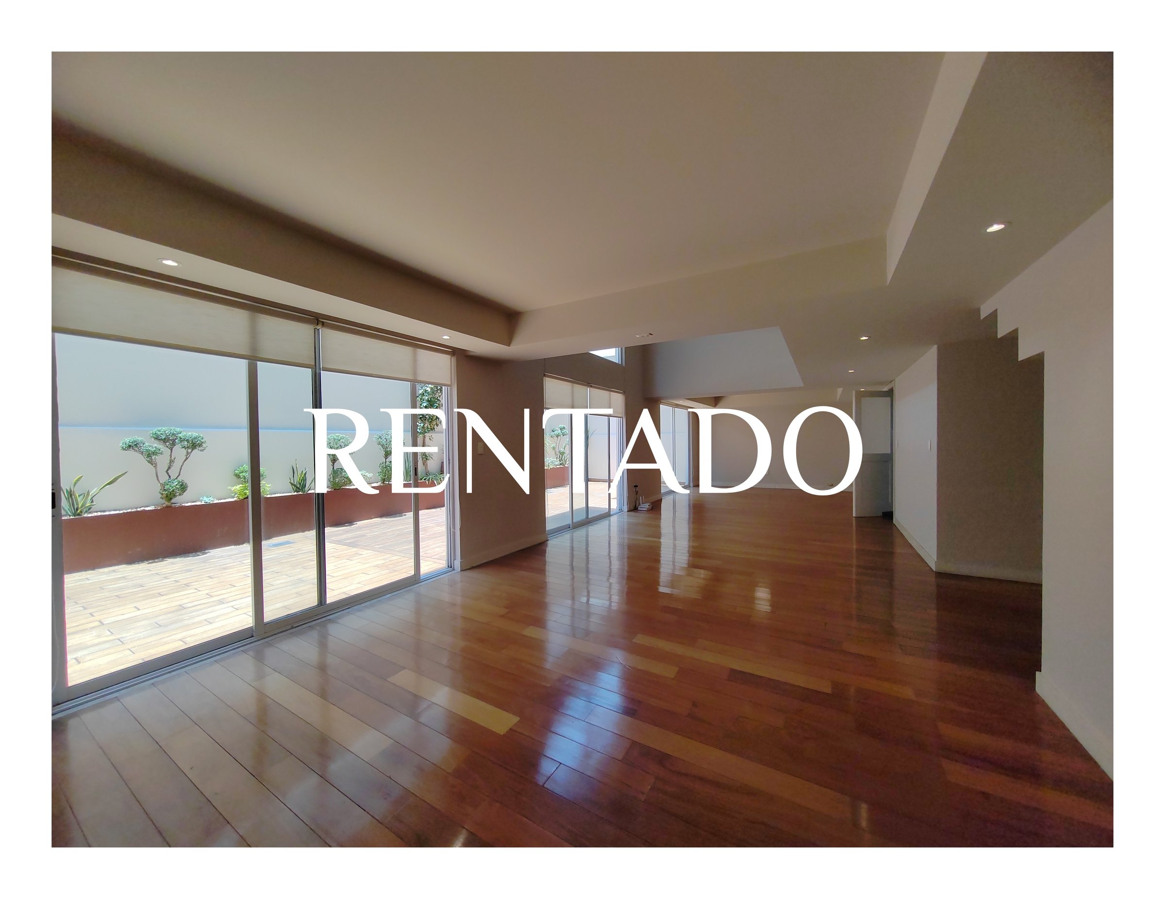 Spacious empty room with wooden flooring, large windows, and RENTADO text overlay, indicating it is rented.