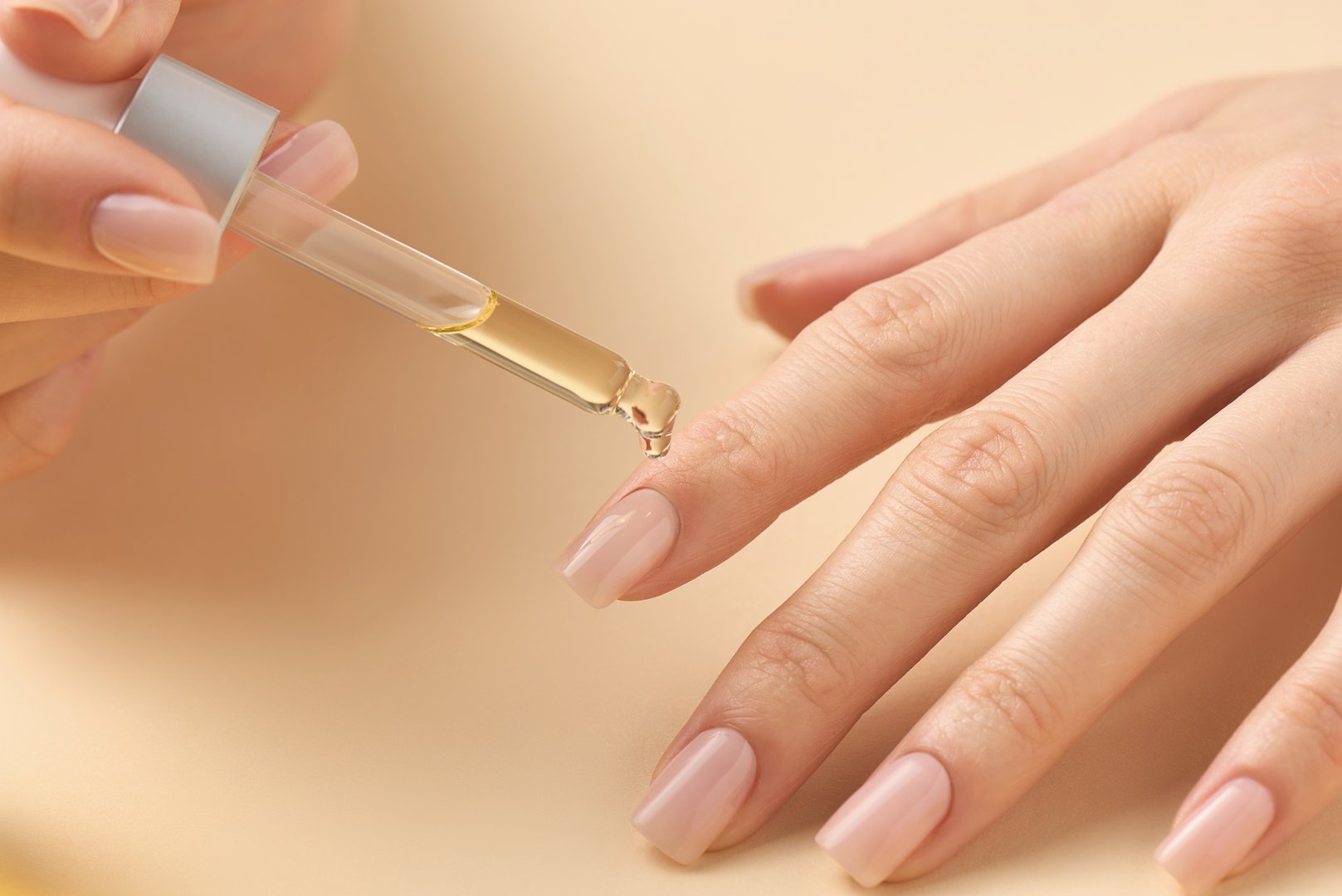 A hand is shown delicately applying a nourishing oil with a dropper to another hand's nails. This self-care moment emphasizes the importance of nail health and grooming.