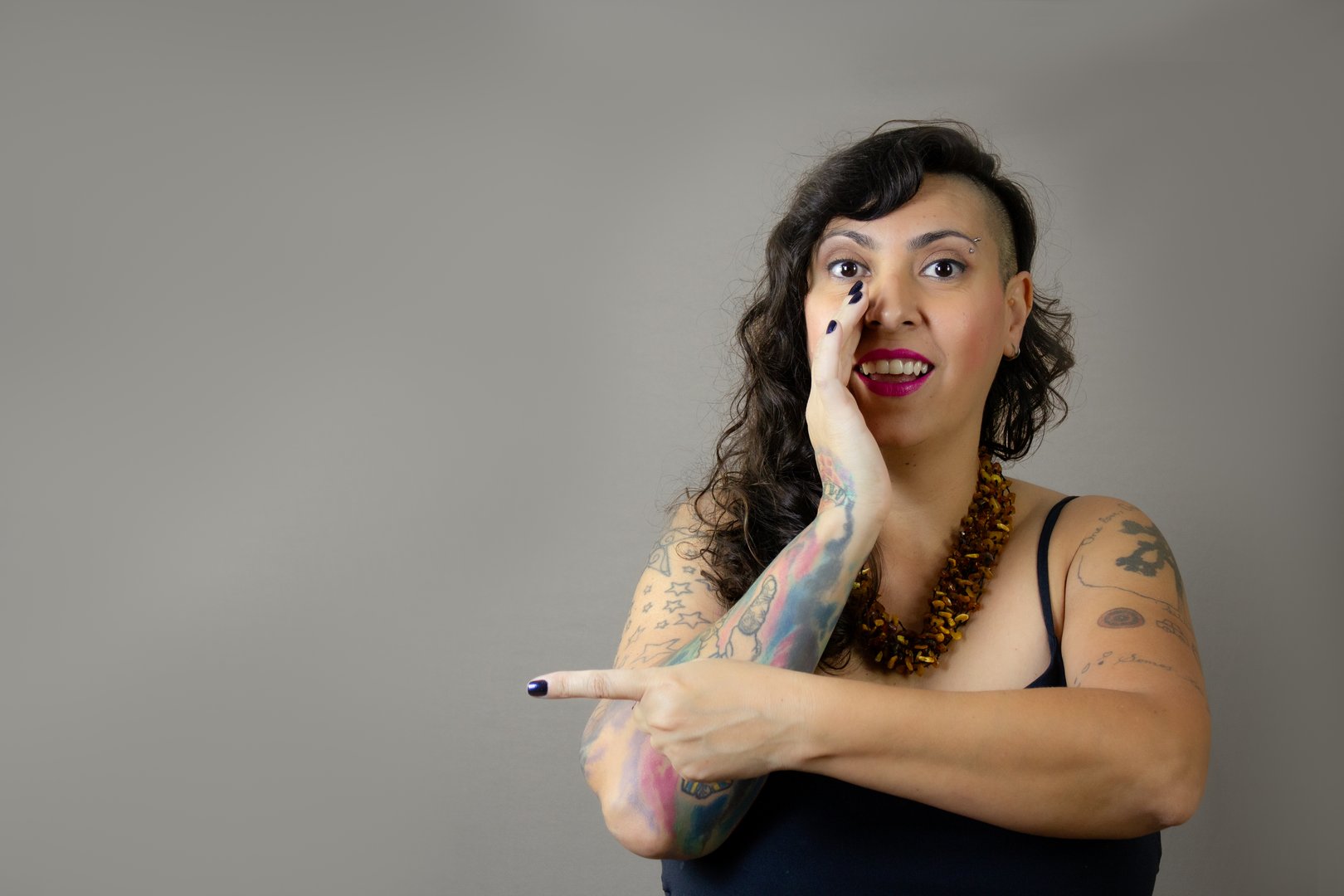 Female model with half-shaved hairstyle and eyebrow piercing. Horizontal studio portrait with neutral gray background.