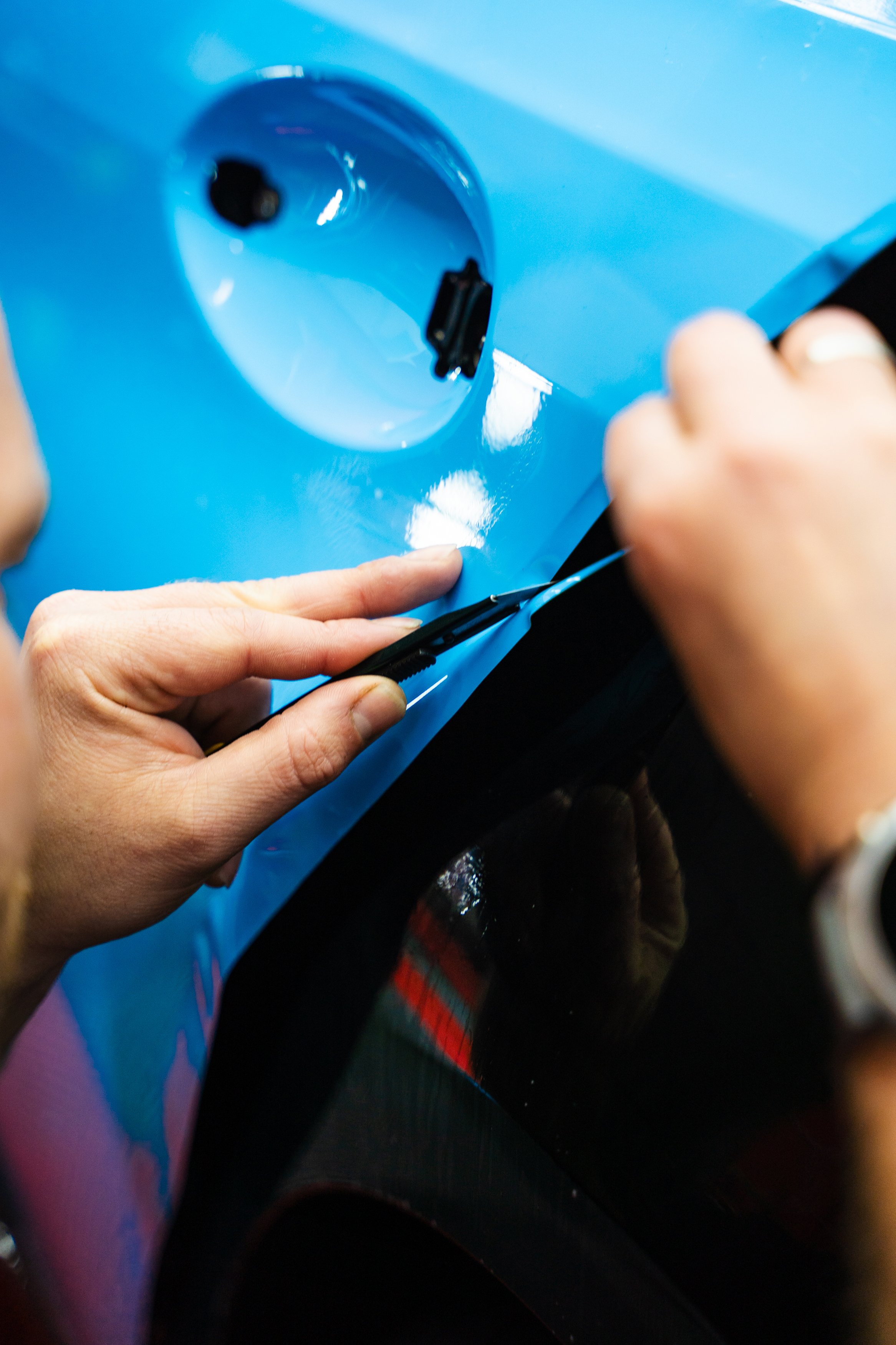 Precision cutting of PPF wrap on car body. Precision PPF wrapping and detailing on car panel using sharp blade to trim wrap with accuracy. Car detailing involves precise vinyl cutting techniques
