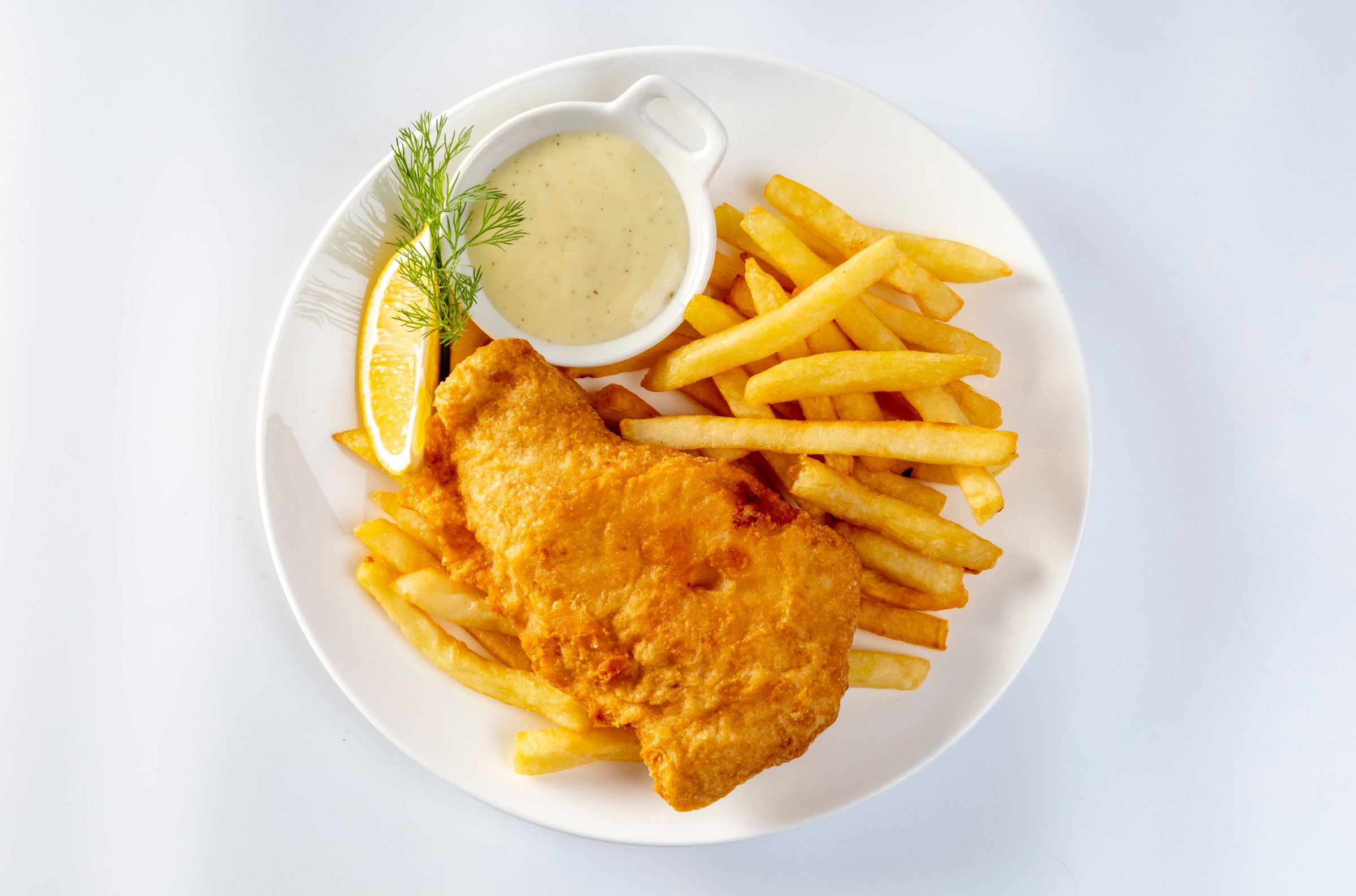 fish and chips served with french fries and tartar sauce with sliced lemon on plate isolated on white background.